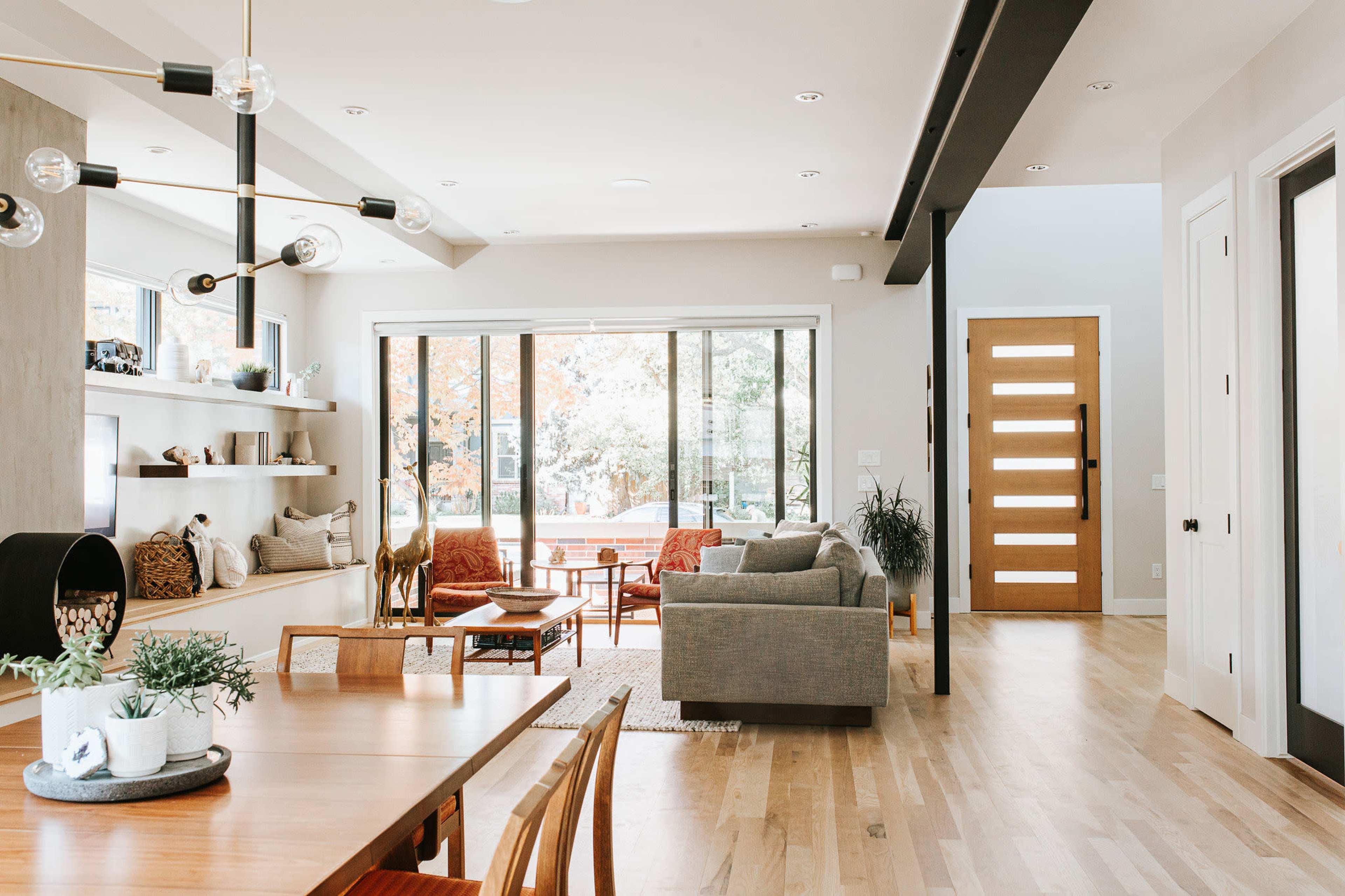 The image shows a modern living space with an open layout, featuring a dining area, a cozy seating area, and large windows that provide natural light.