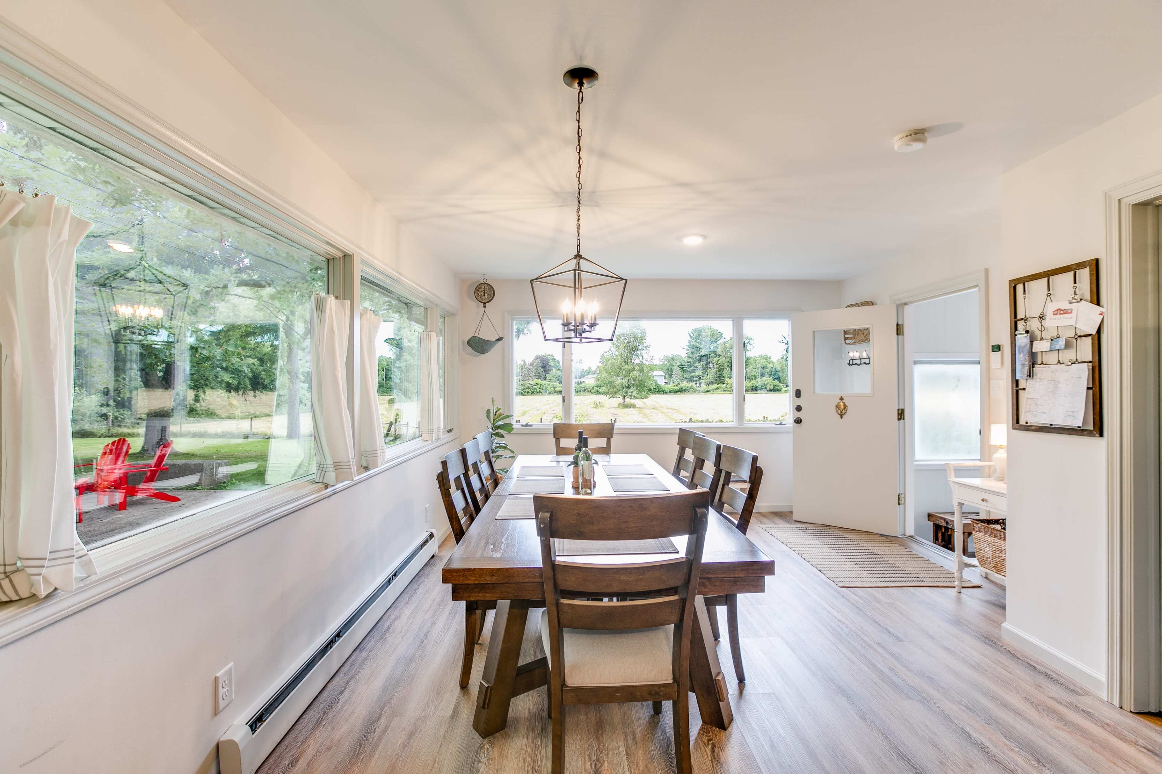 A spacious dining area features a wooden table surrounded by chairs, with large windows providing a view of an outdoor landscape.