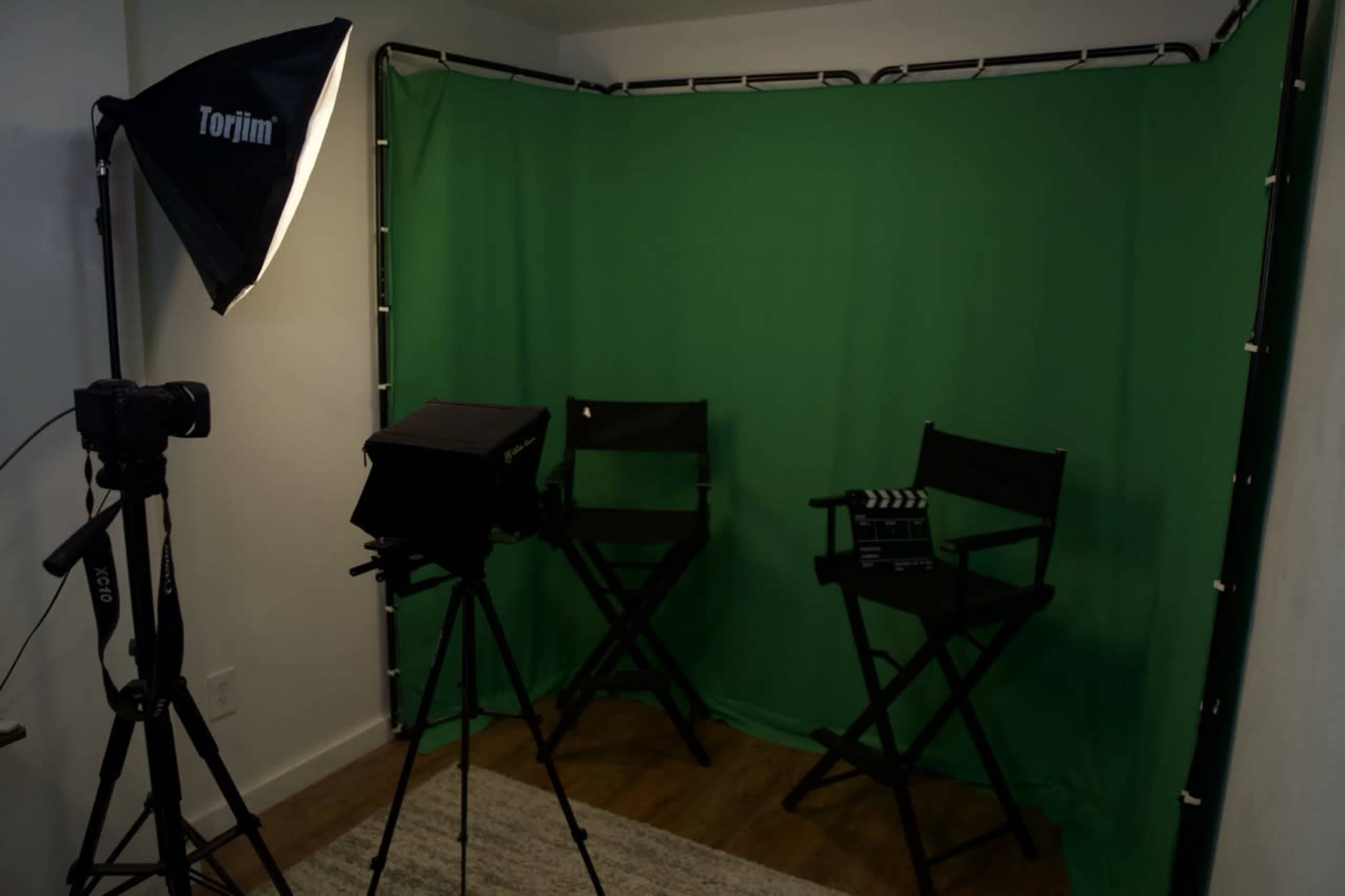 The image shows a film setup featuring two director's chairs in front of a green screen, with a camera and light positioned on the side.