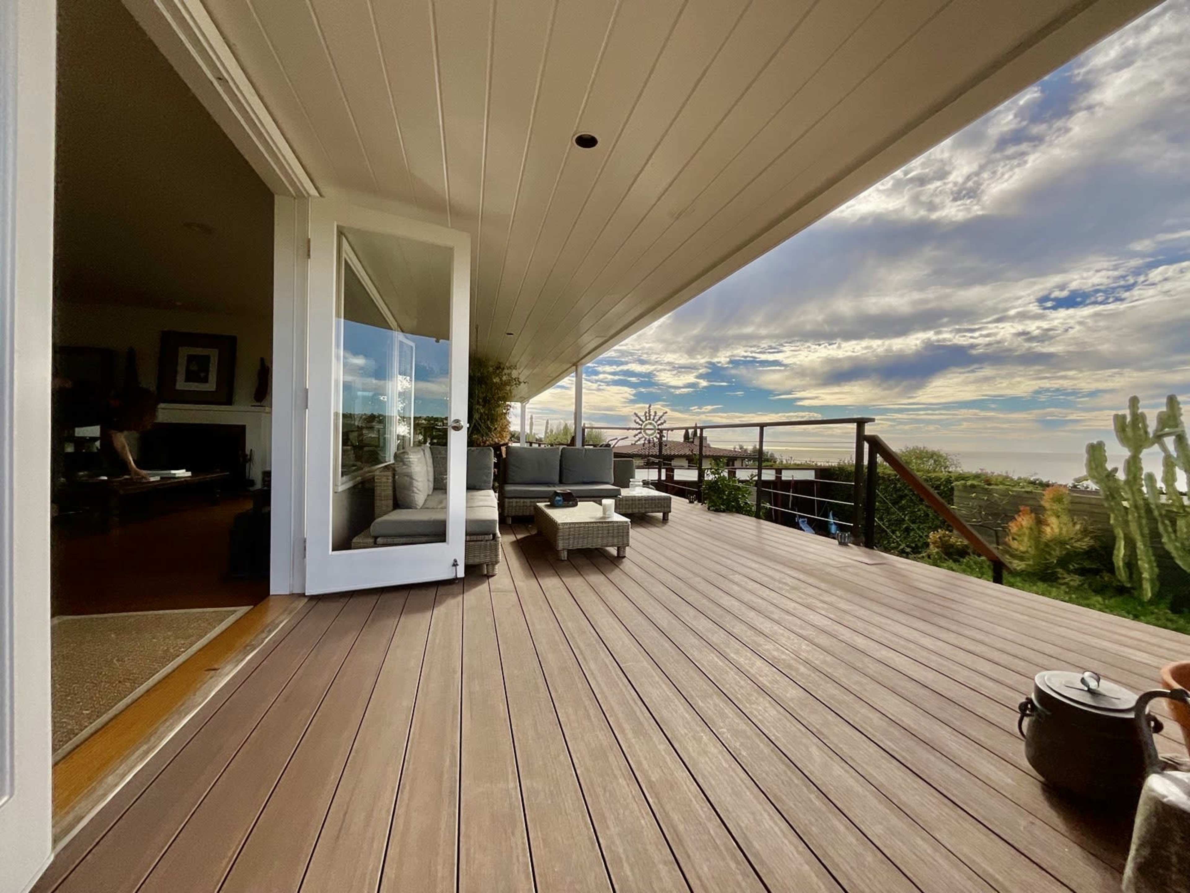 The image shows a spacious outdoor deck with seating arrangements, overlooking a landscape under a partly cloudy sky.