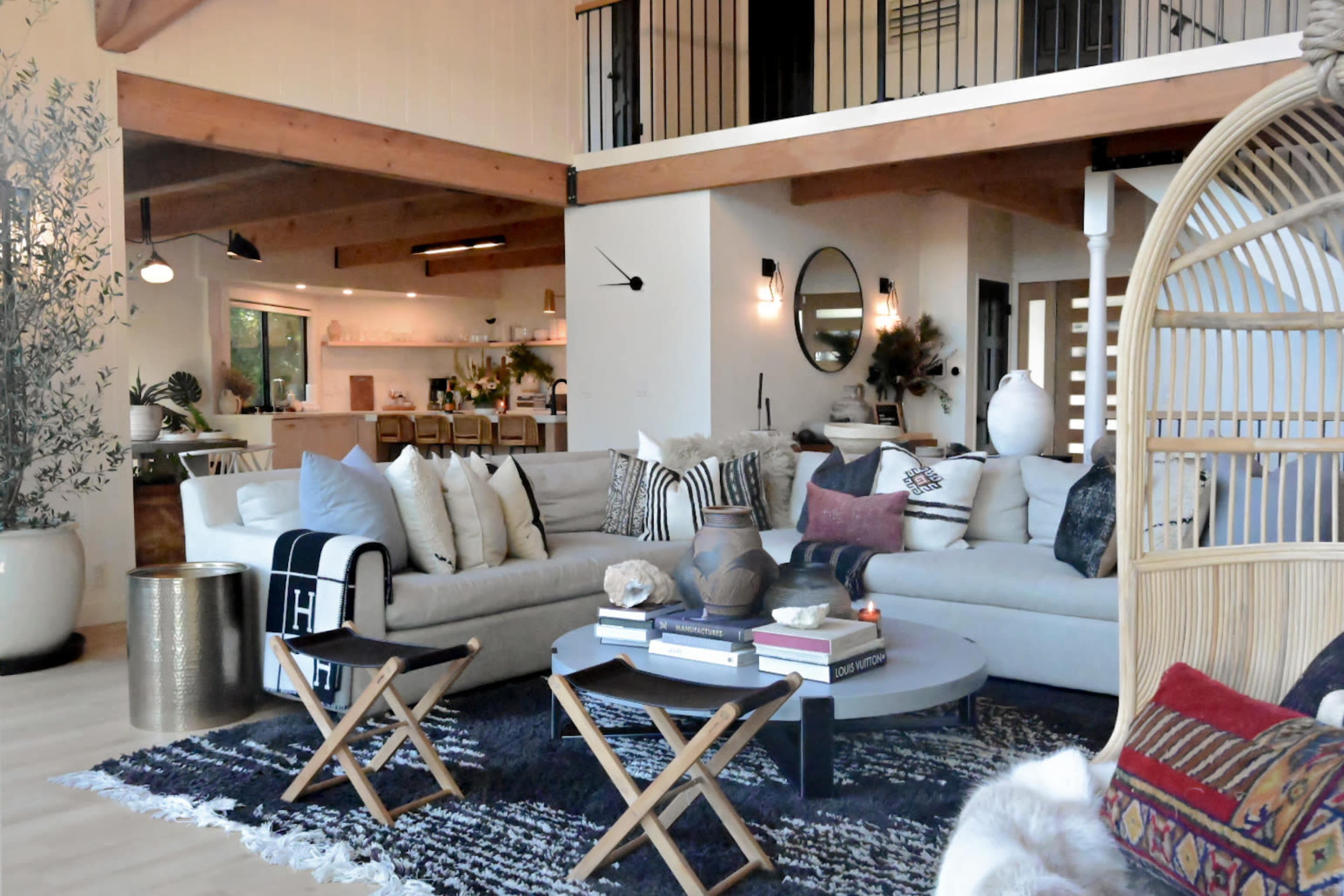 A spacious living room with a large sectional sofa, a round coffee table, and various decorative elements against a backdrop of wood beams and an open kitchen.