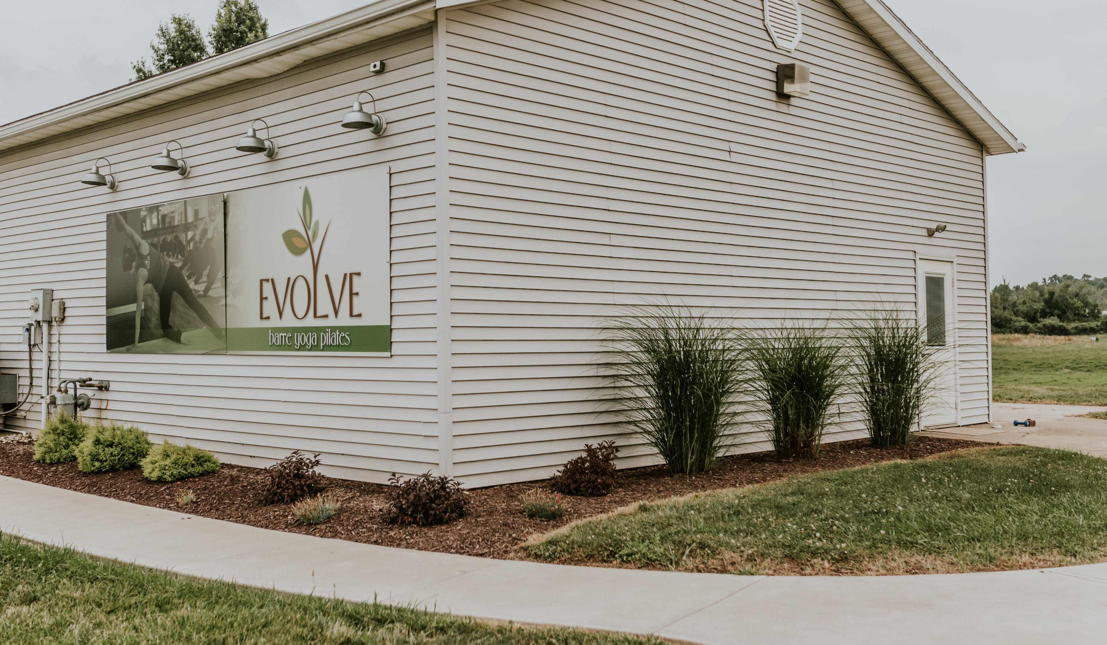 A single-story building with a sign reading "EVOLVE" and landscaped plants is shown against a grassy field.