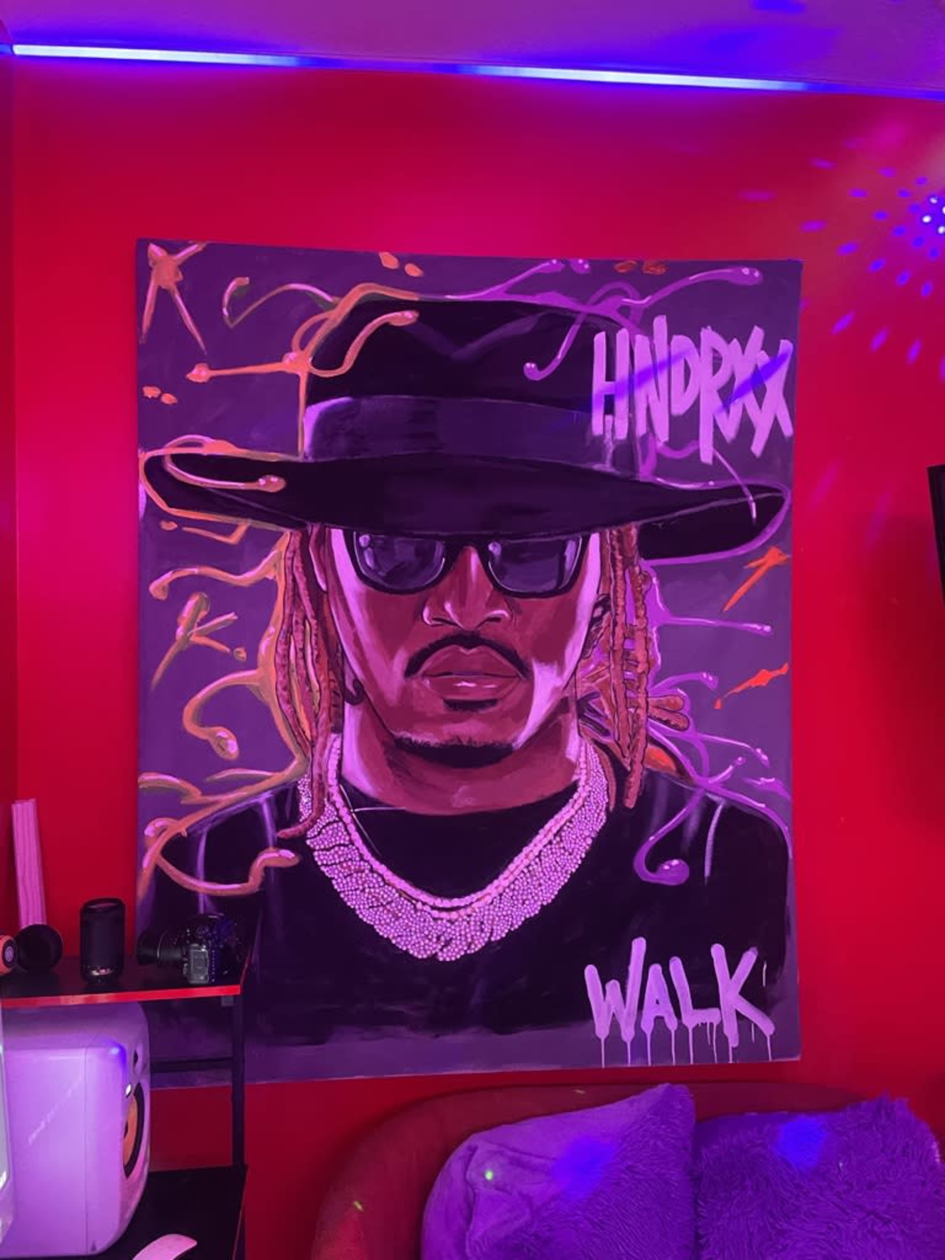 The image shows a large mural of a man wearing sunglasses and a wide-brimmed hat, hanging on a vibrant red wall.