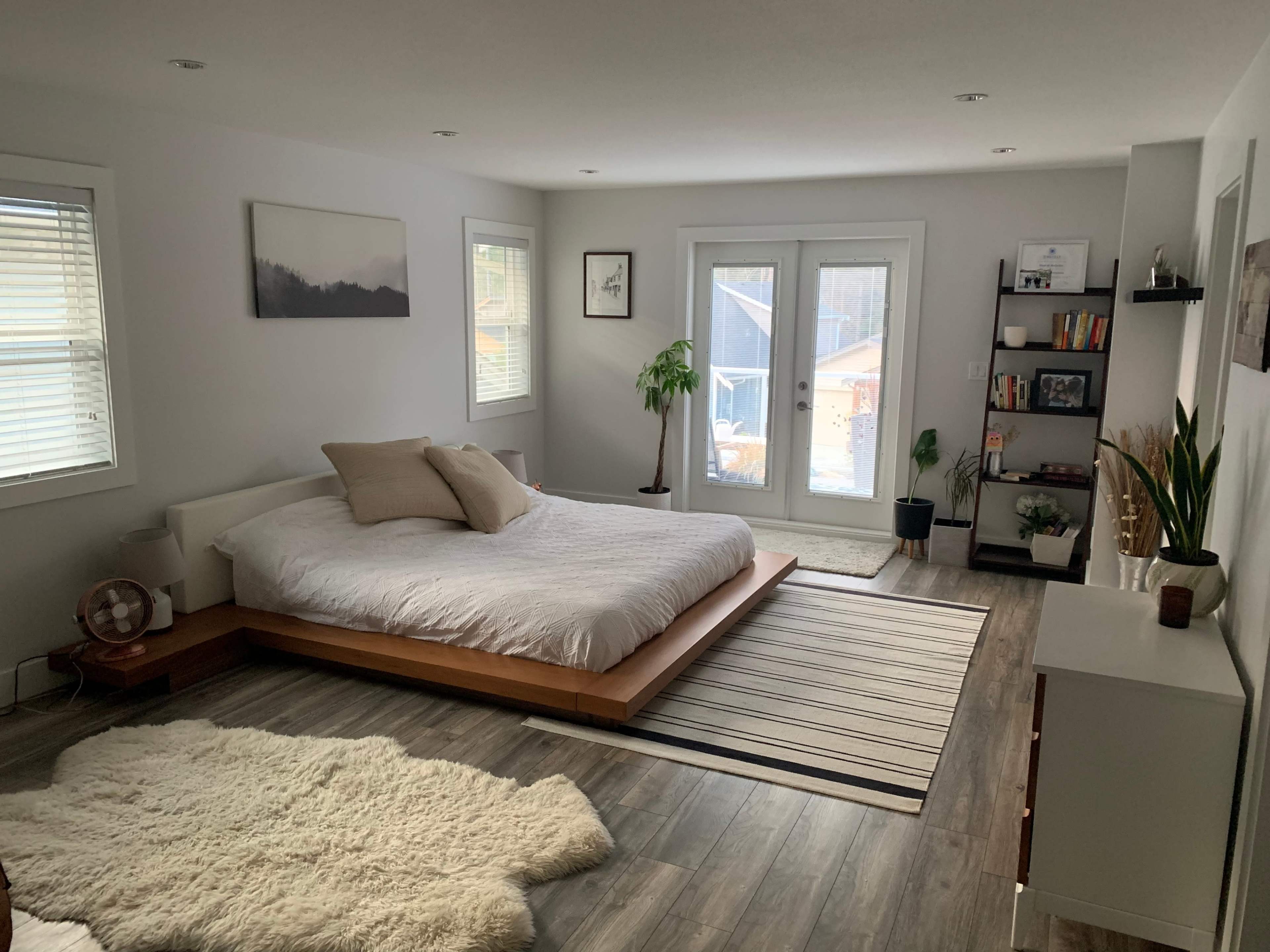 A modern bedroom featuring a low-profile bed, a large window with a view, and a minimalist design with wooden and neutral elements.