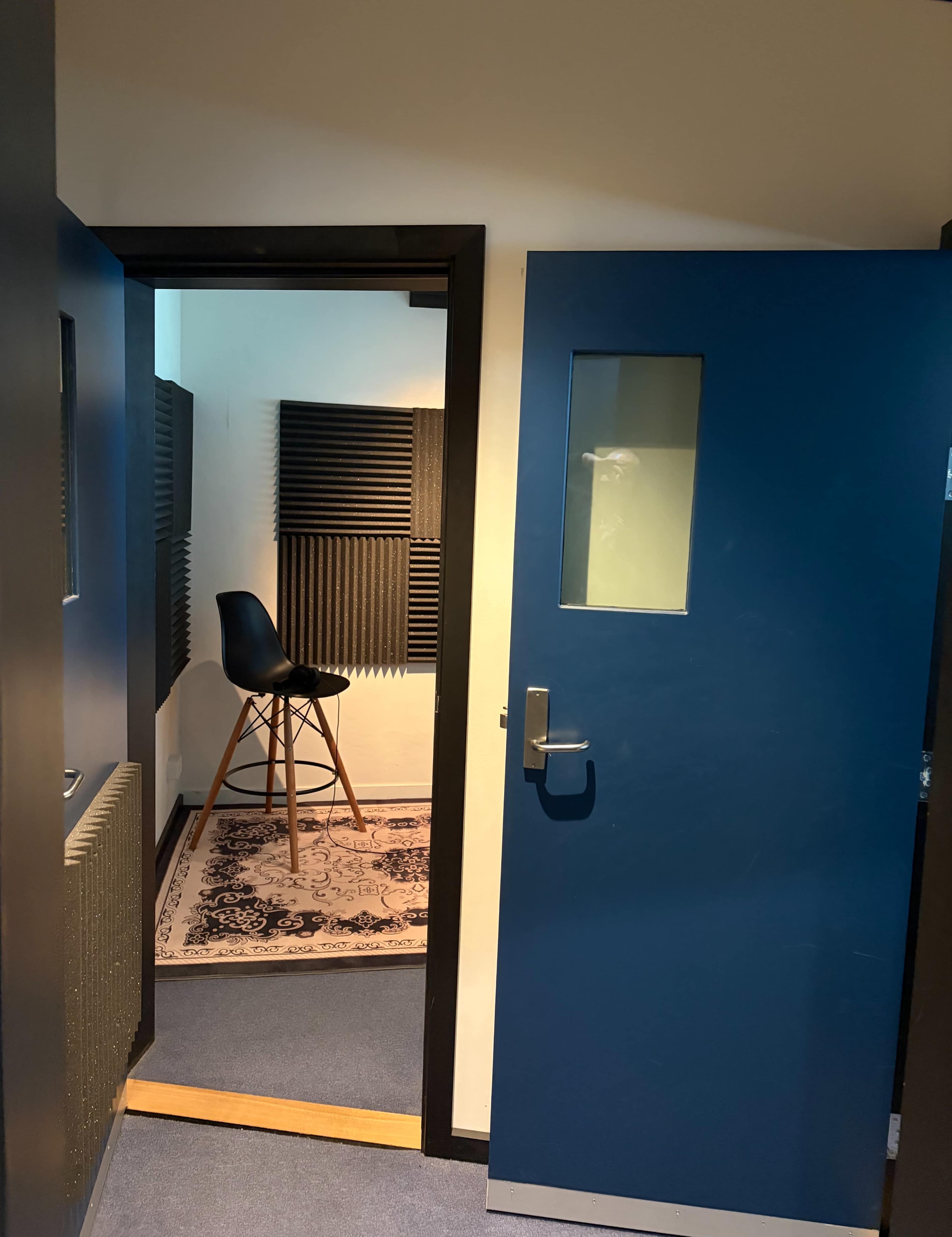 The image shows a doorway leading into a soundproof recording booth, with a chair positioned inside and acoustic panels on the walls.