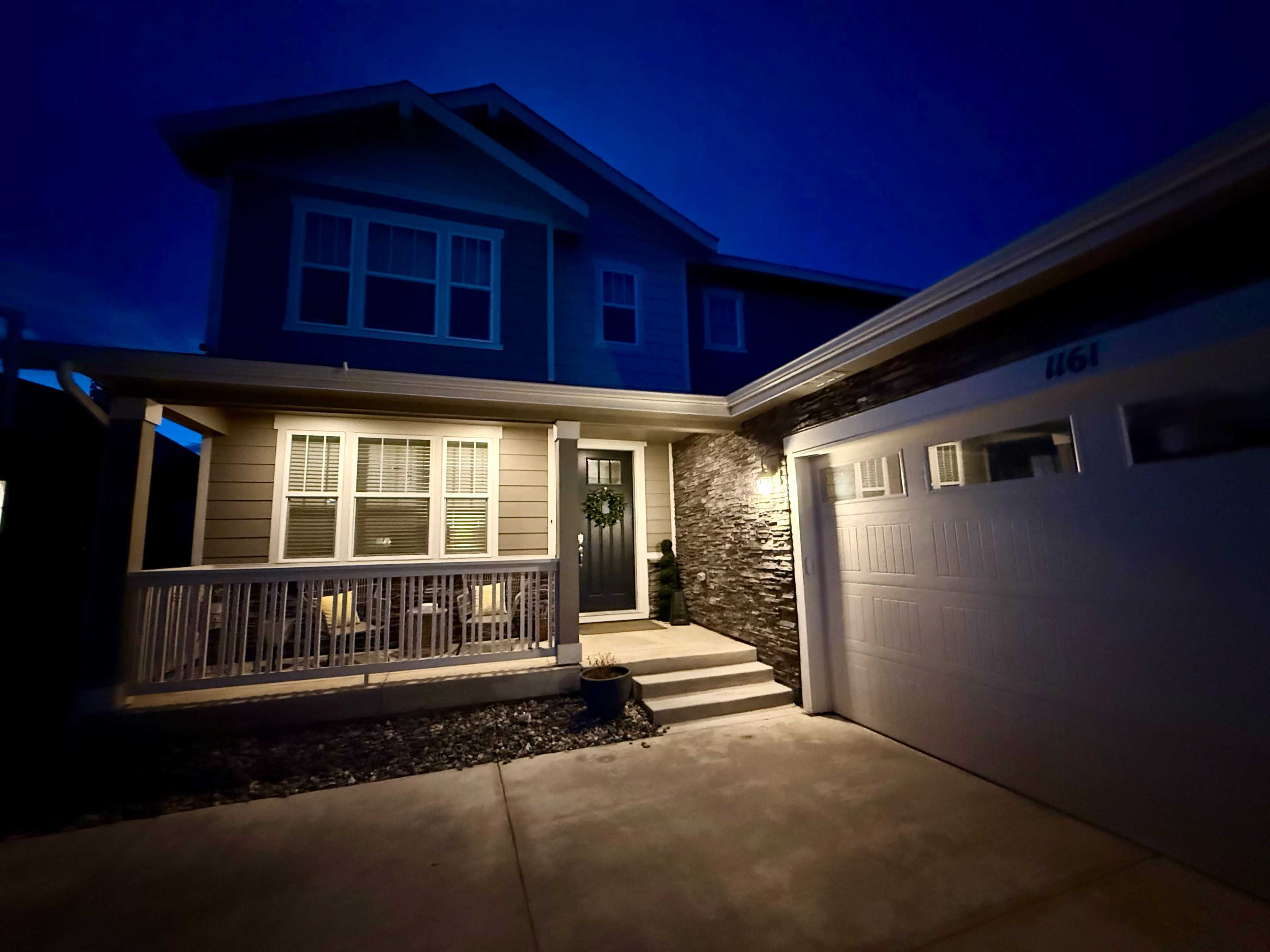 A two-story house with a front porch and a garage is illuminated at dusk.