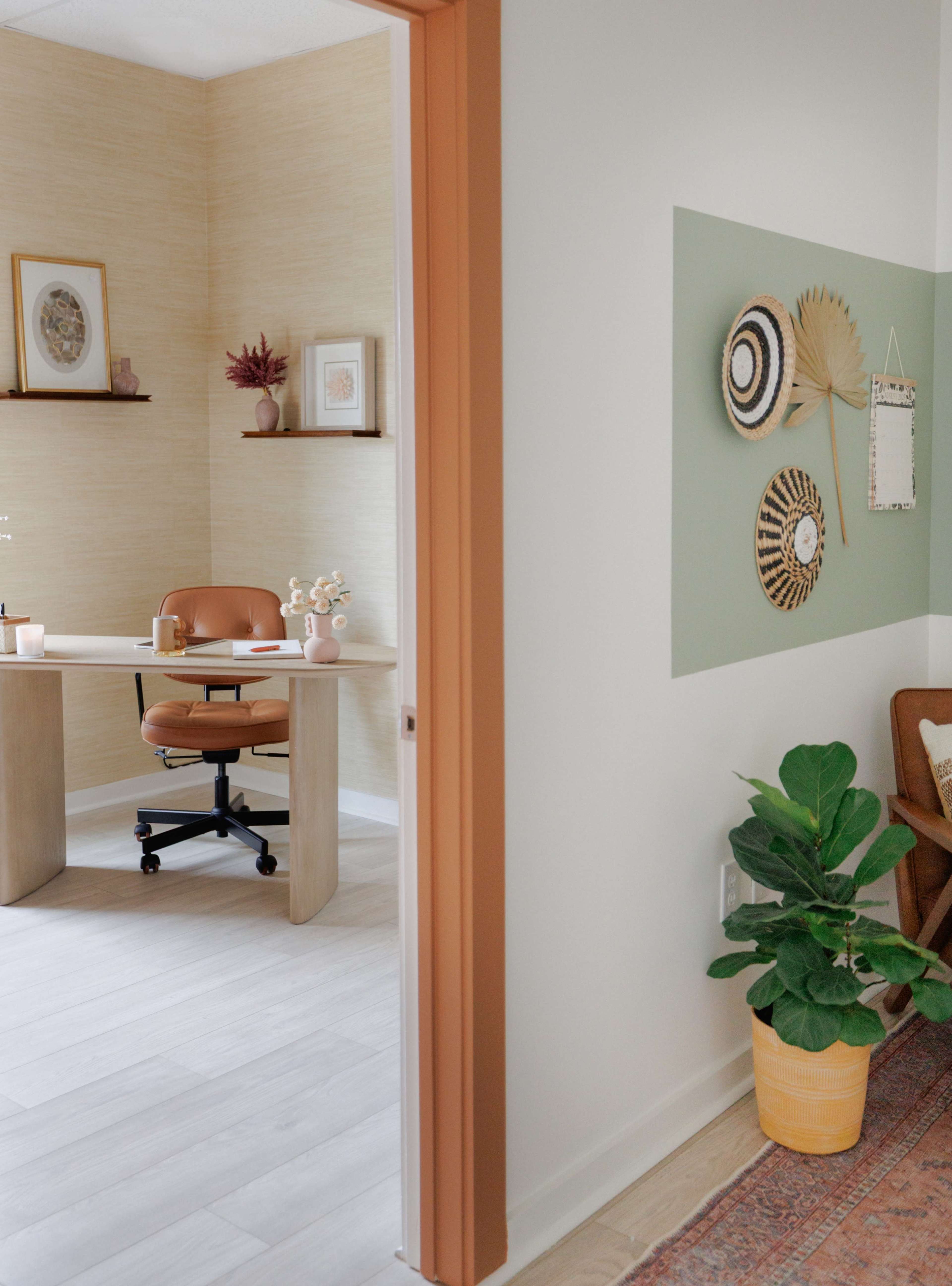 The image shows a well-lit office space featuring a desk with a brown chair, shelves with decorative items, and a green accent wall with circular wall decor.