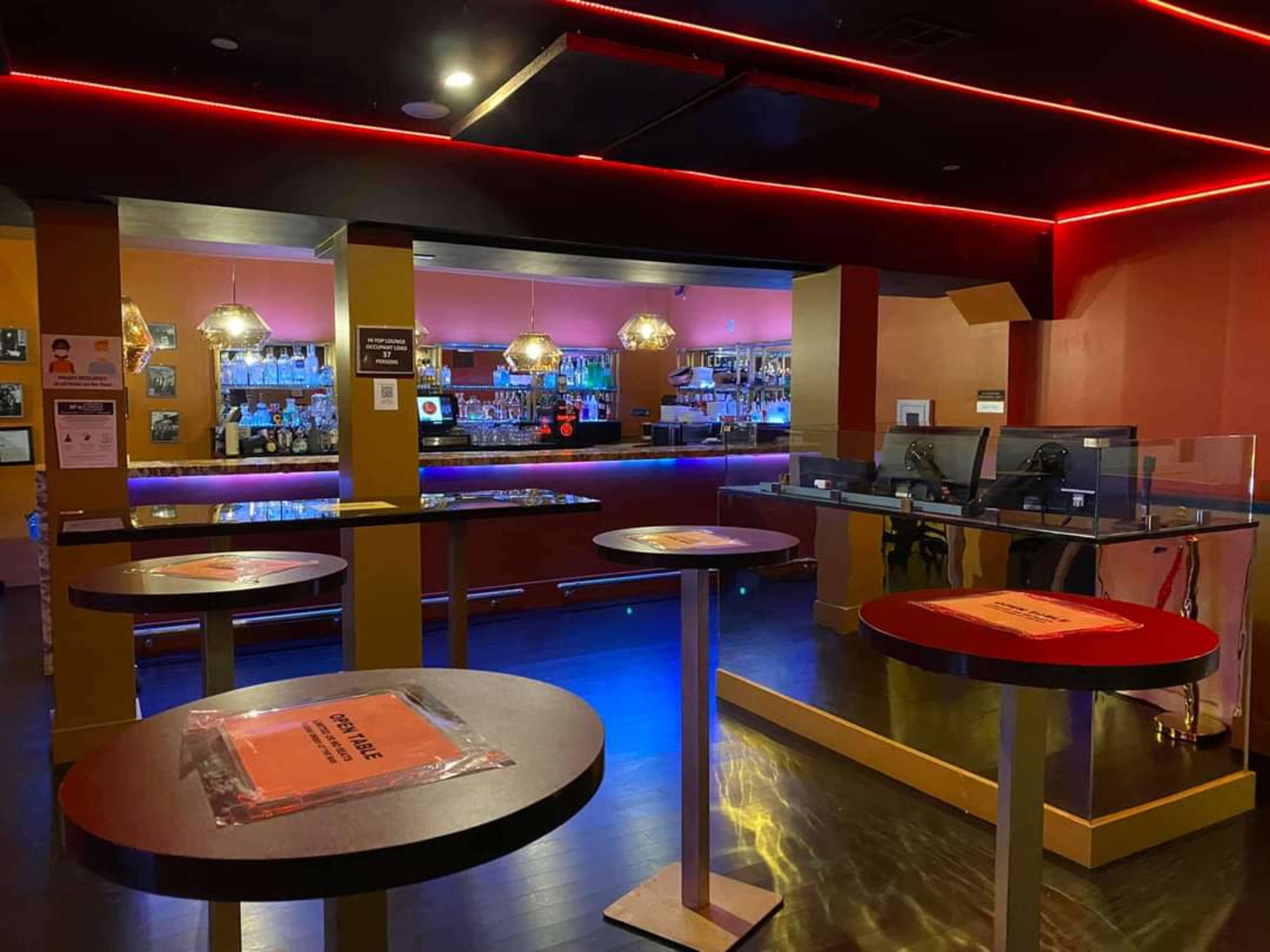 The image shows a bar area with several tables and a counter, featuring bright red lighting and a variety of bottles displayed on the shelves behind the bar.