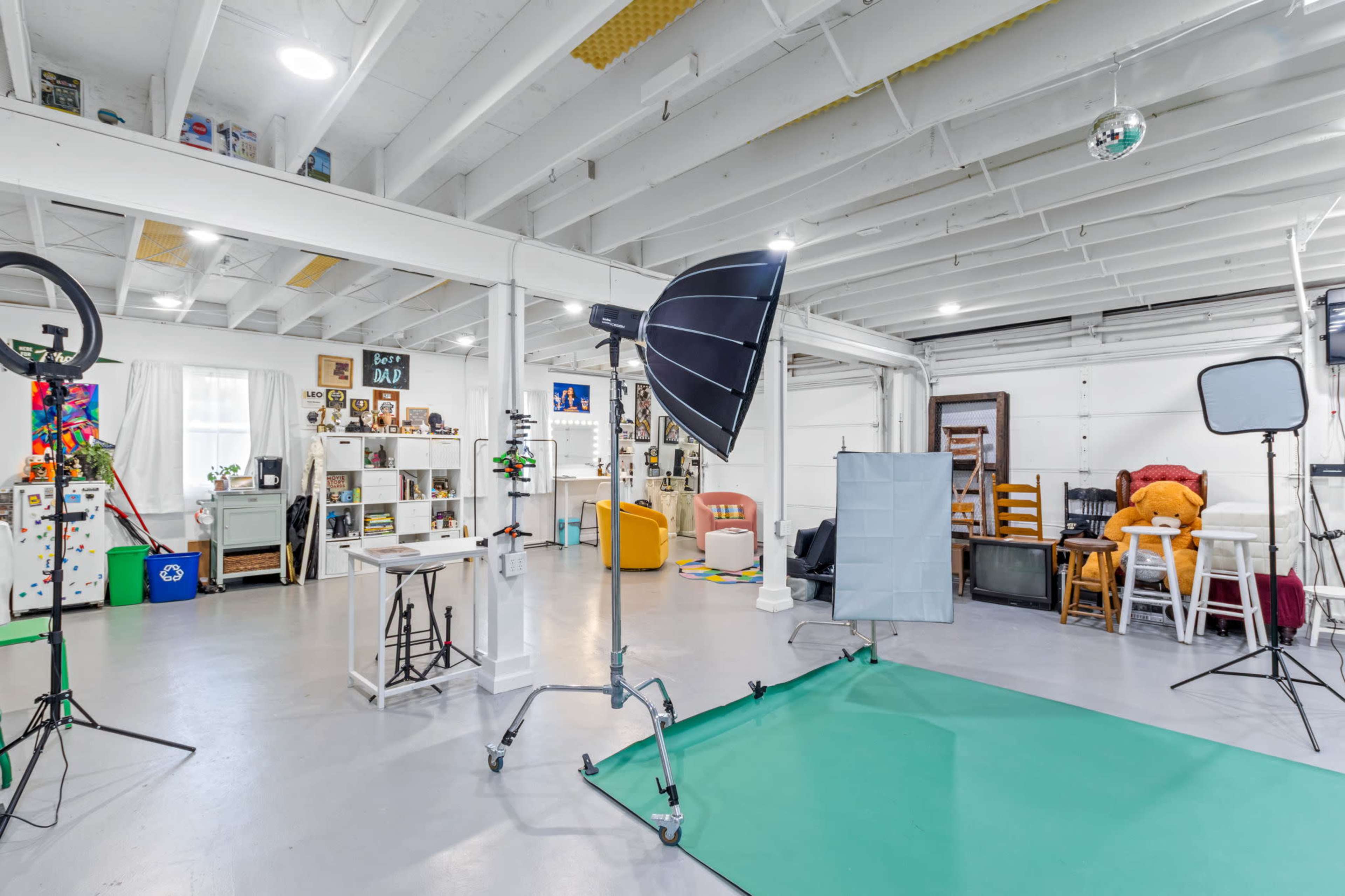The image shows a studio space with various photography equipment, including light sources and backdrops, alongside shelves and furniture arranged in a tidy manner.