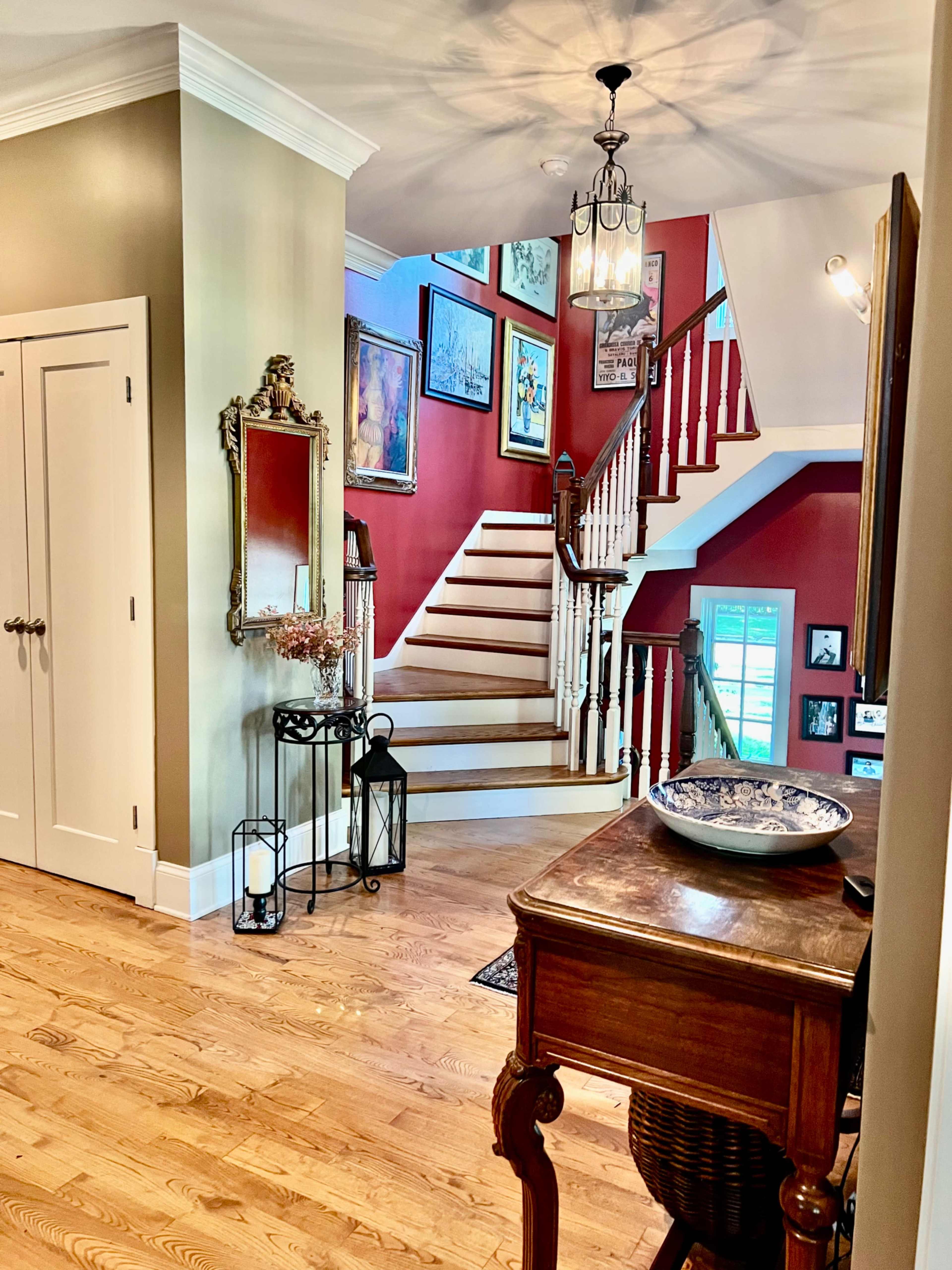 The image shows a well-lit hallway leading to a staircase, with decorative artwork on the walls and furniture placed along the floor.
