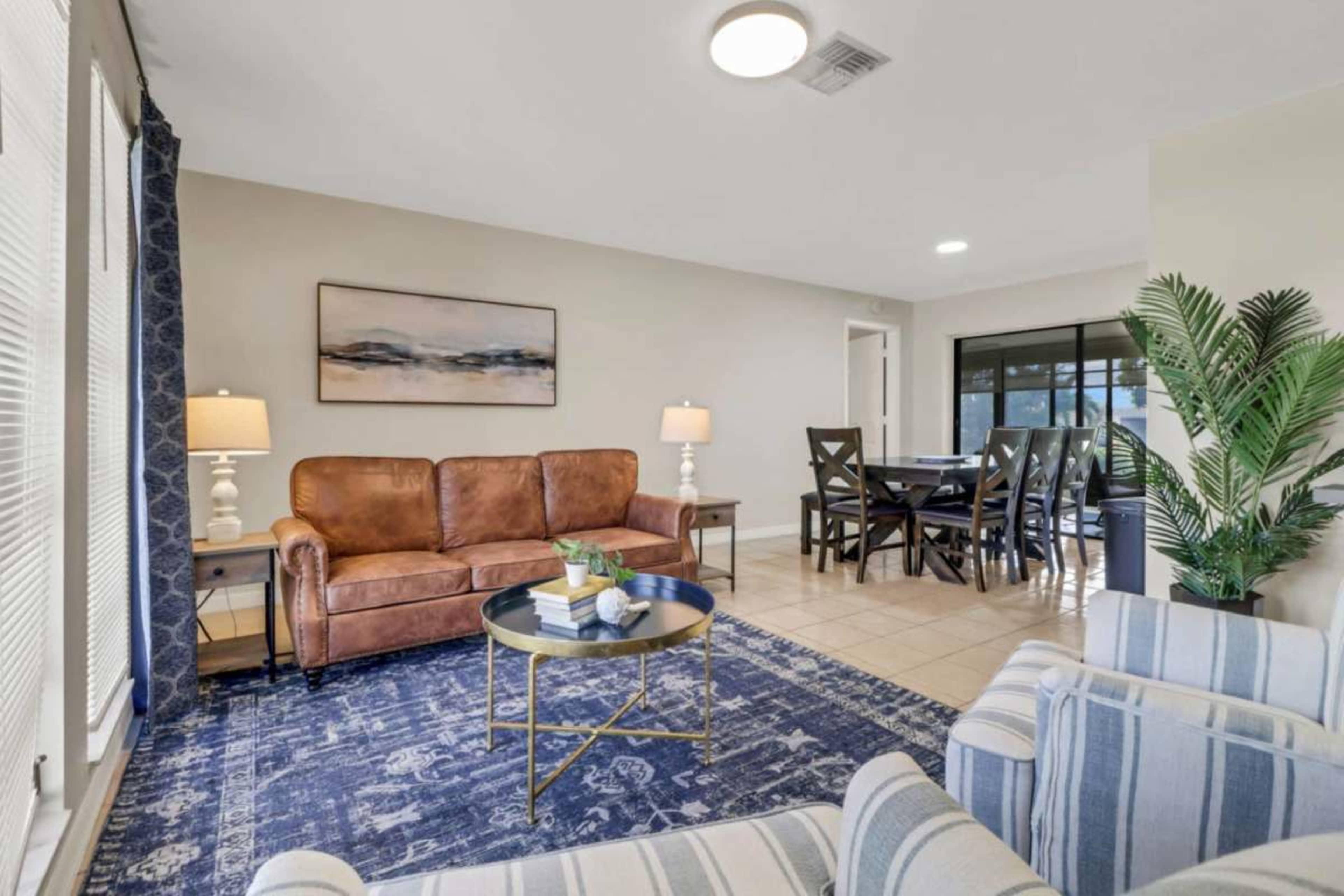 A modern living room featuring a brown leather sofa, striped armchairs, a round coffee table, and a dining area with a dark wood table and chairs.