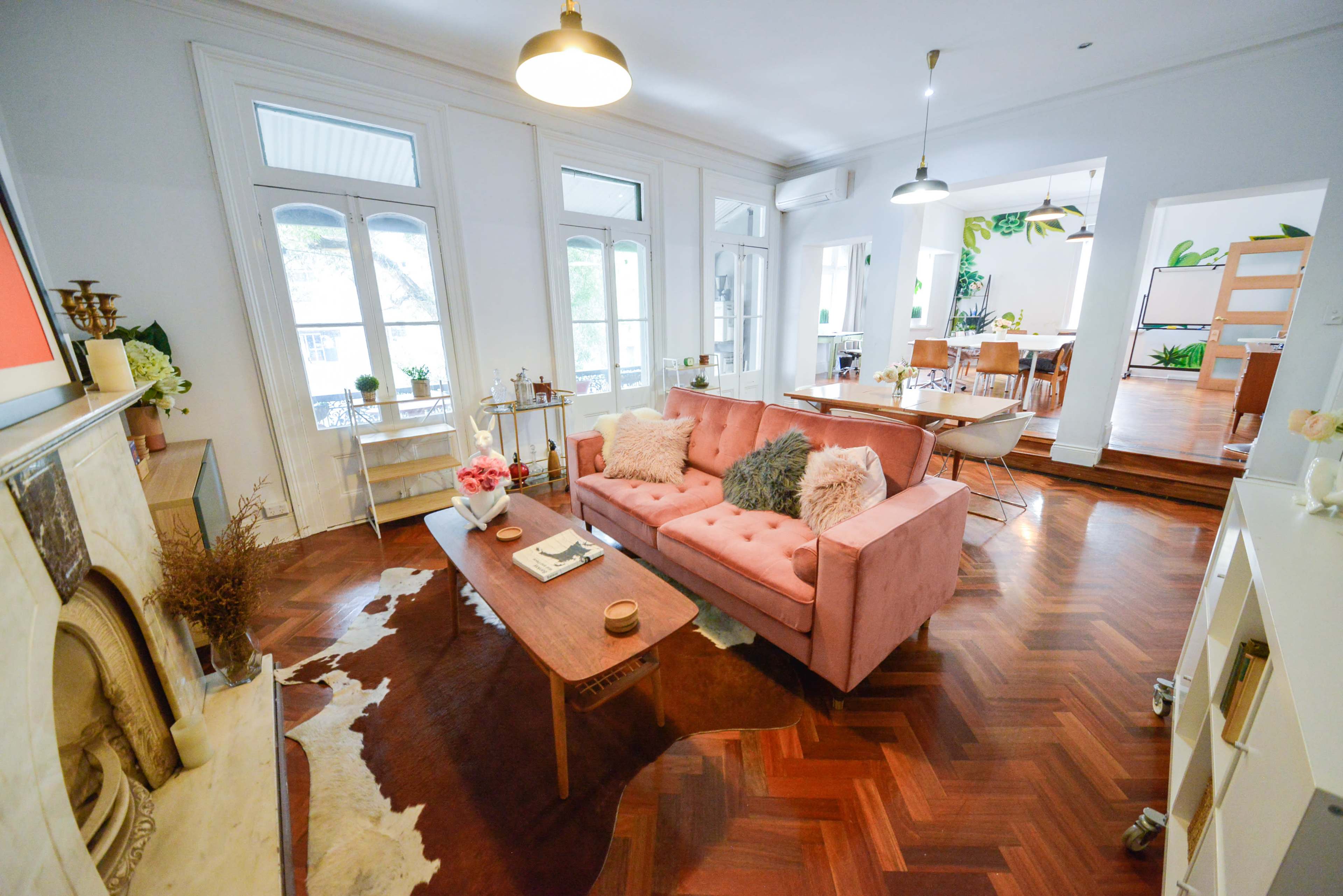 A modern living room with a pink sofa, wooden coffee table, and large windows that allow natural light to enter.