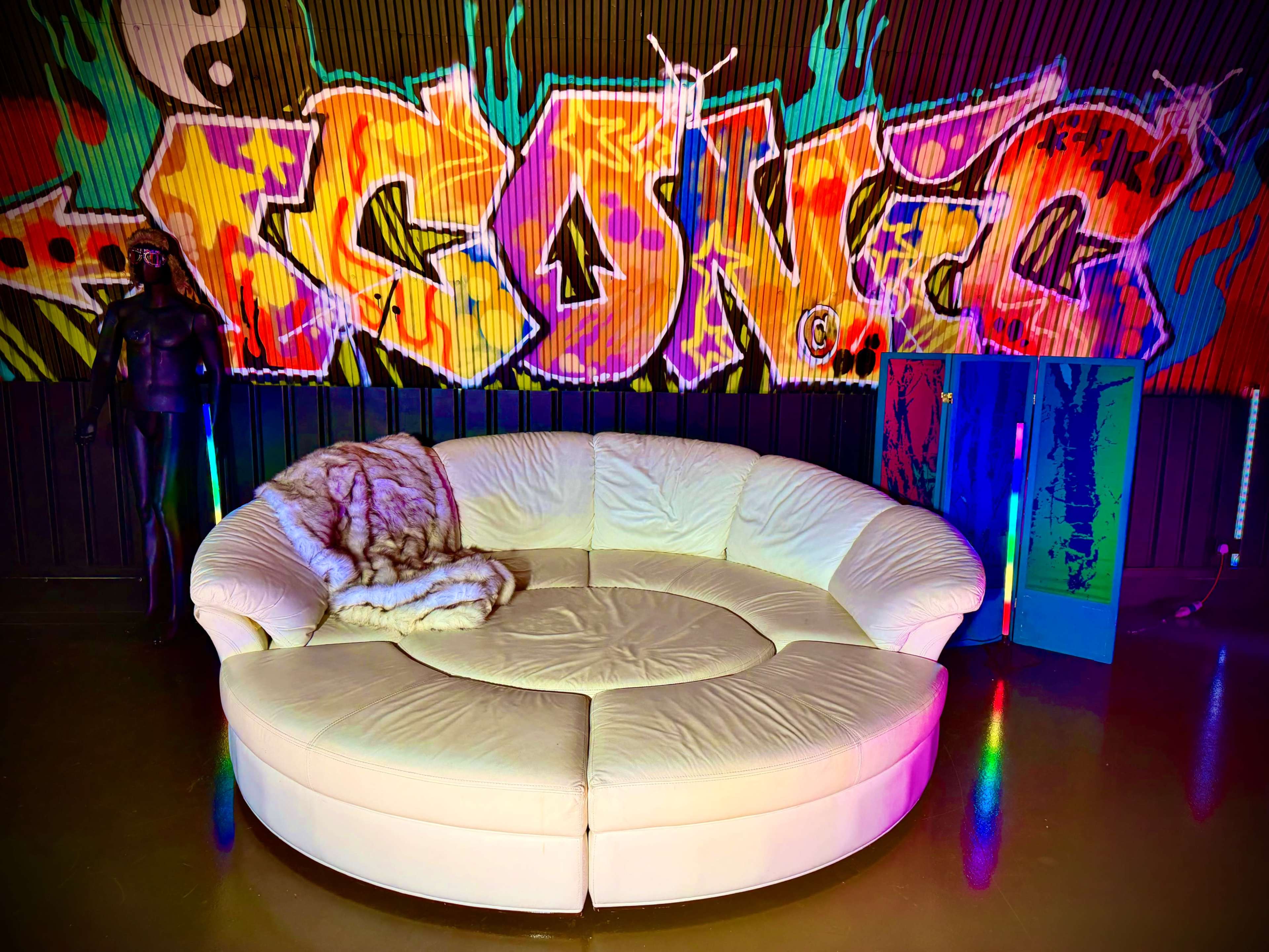 A curved white sofa is positioned in front of a vibrant graffiti mural on a black wall.