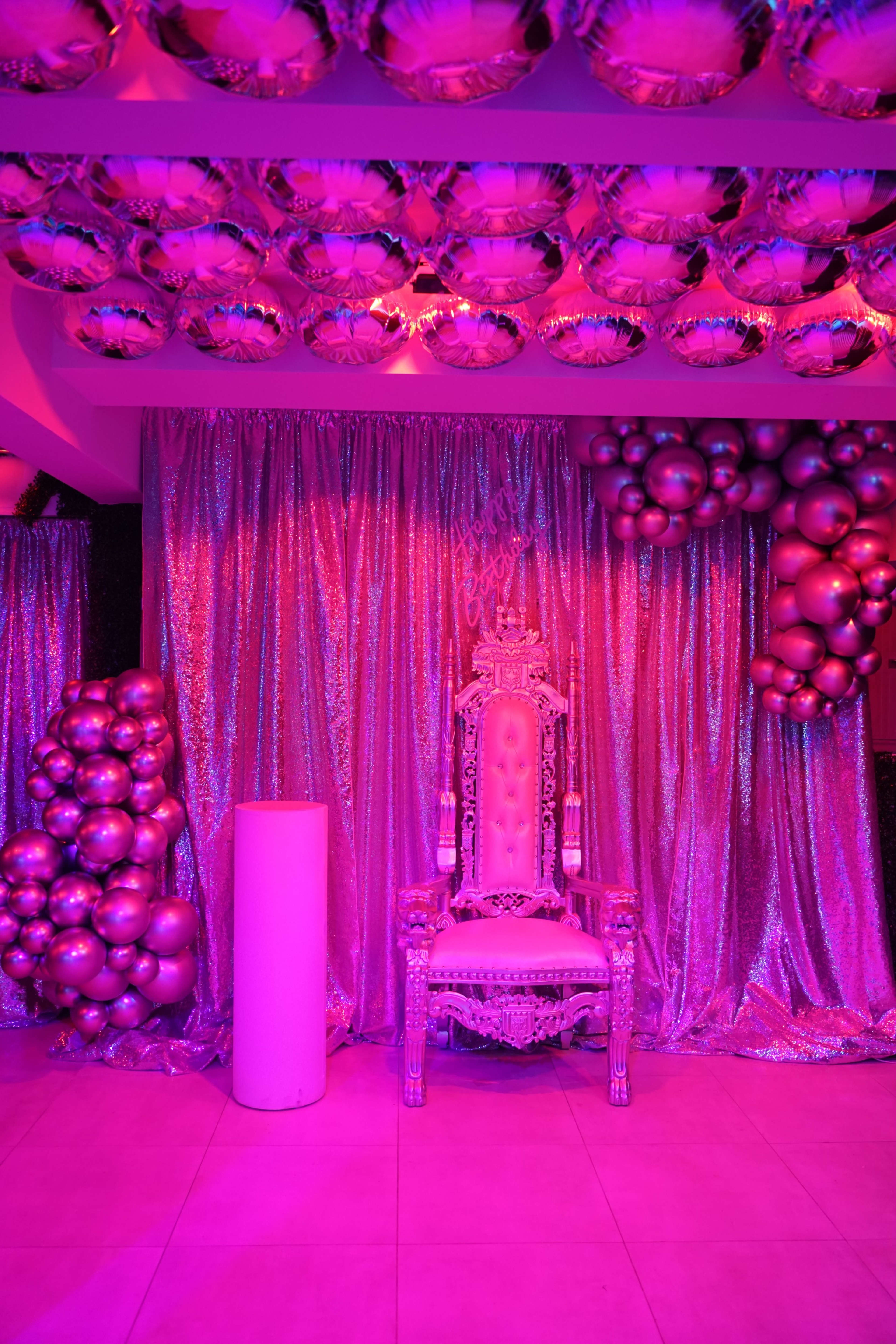A lavish throne surrounded by shimmering pink curtains and balloon decorations fills the room.