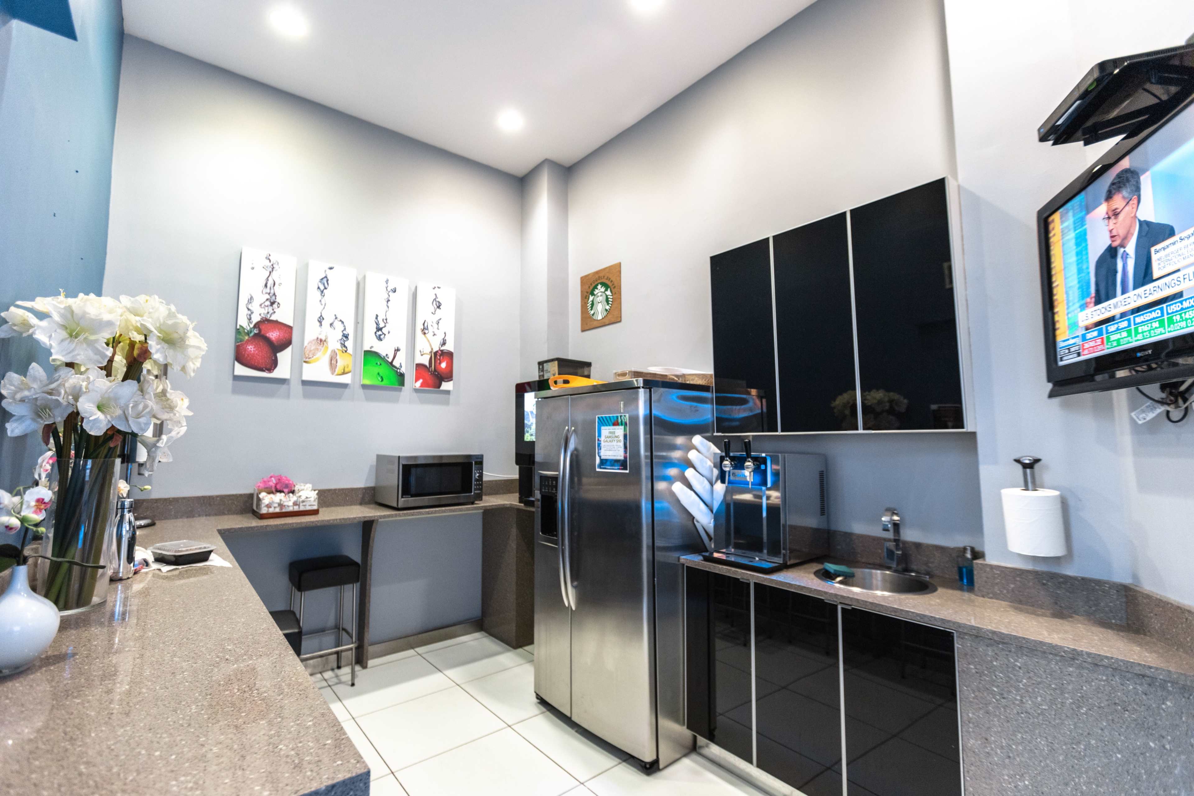 A modern kitchenette with stainless steel appliances, a microwave, and a television mounted on the wall.