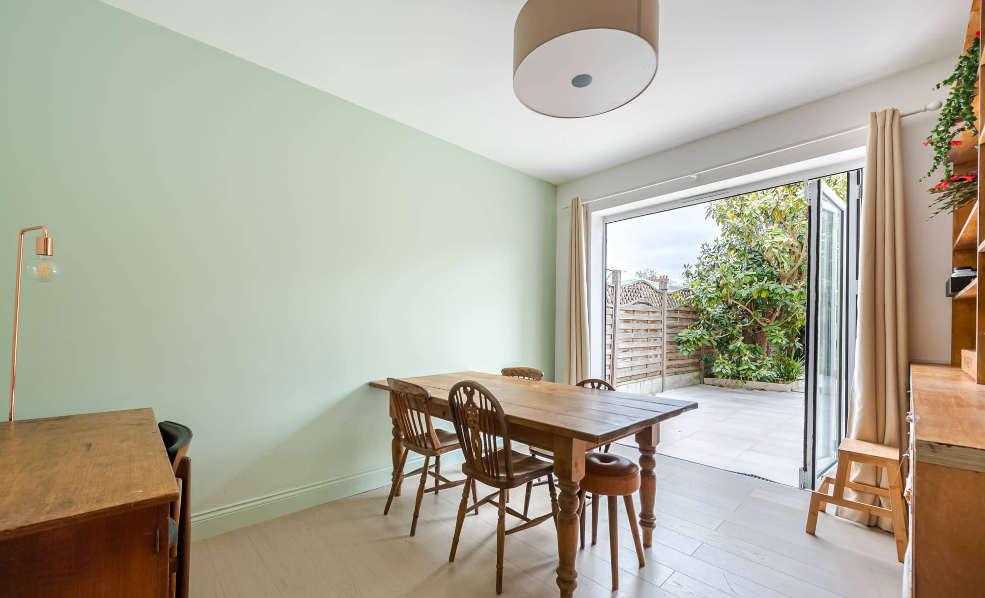 A small dining area features a wooden table with four chairs and a door opening to a garden.