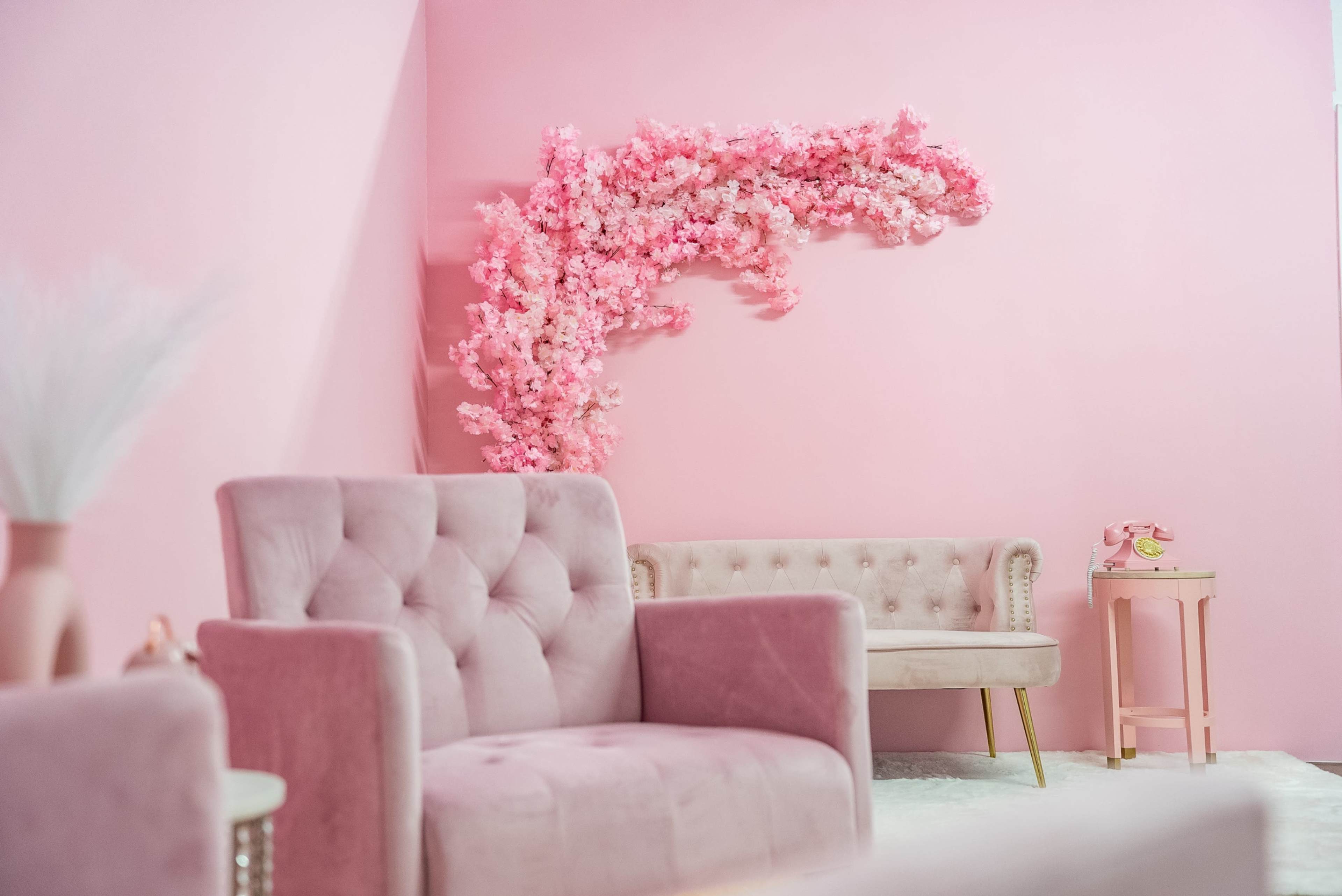A cozy pink room featuring two plush chairs, a small side table, and a decorative wall covered in pink flowers.