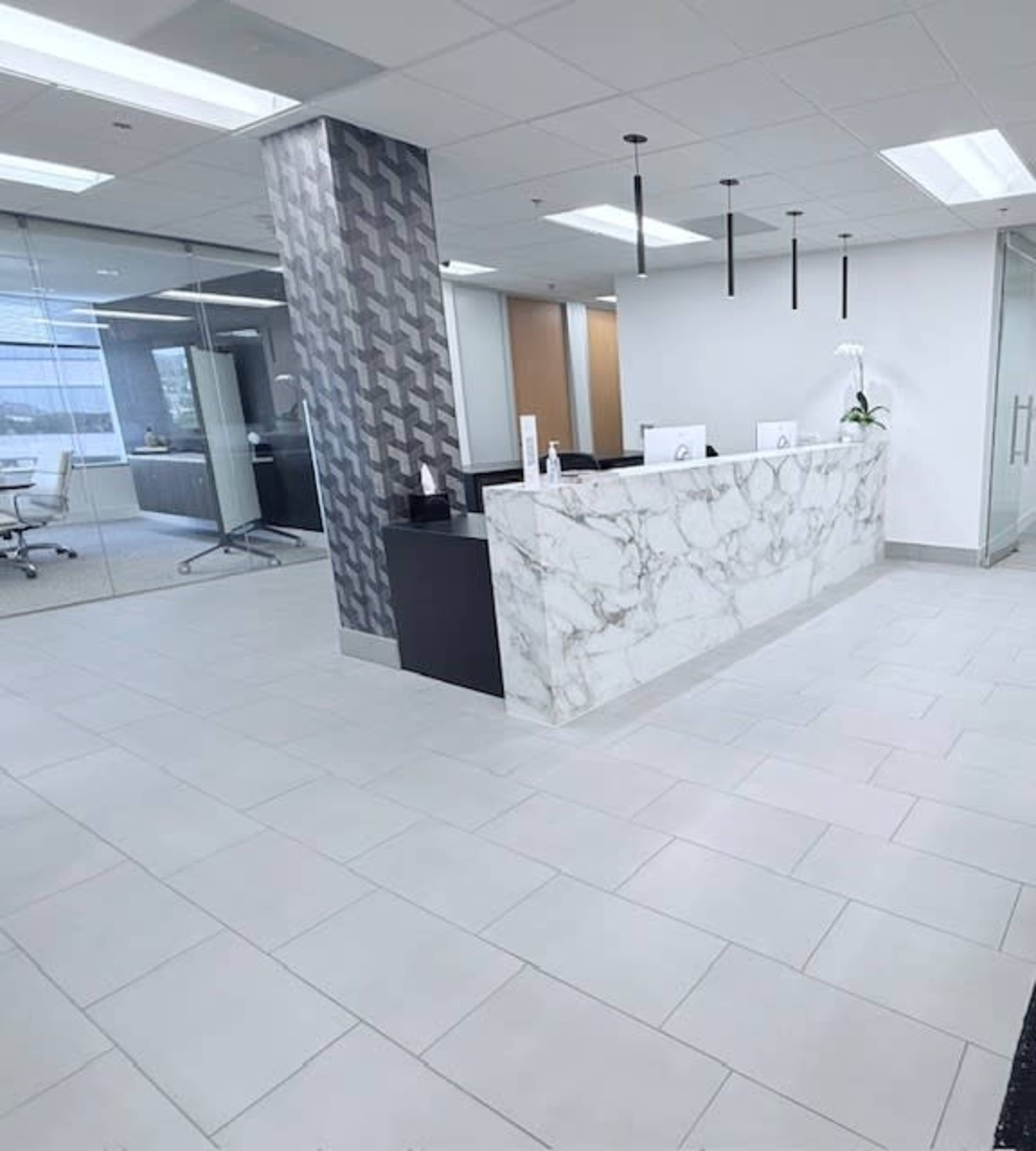 The image shows a modern office reception area with a marble reception desk, tiled flooring, and a glass-walled meeting room in the background.