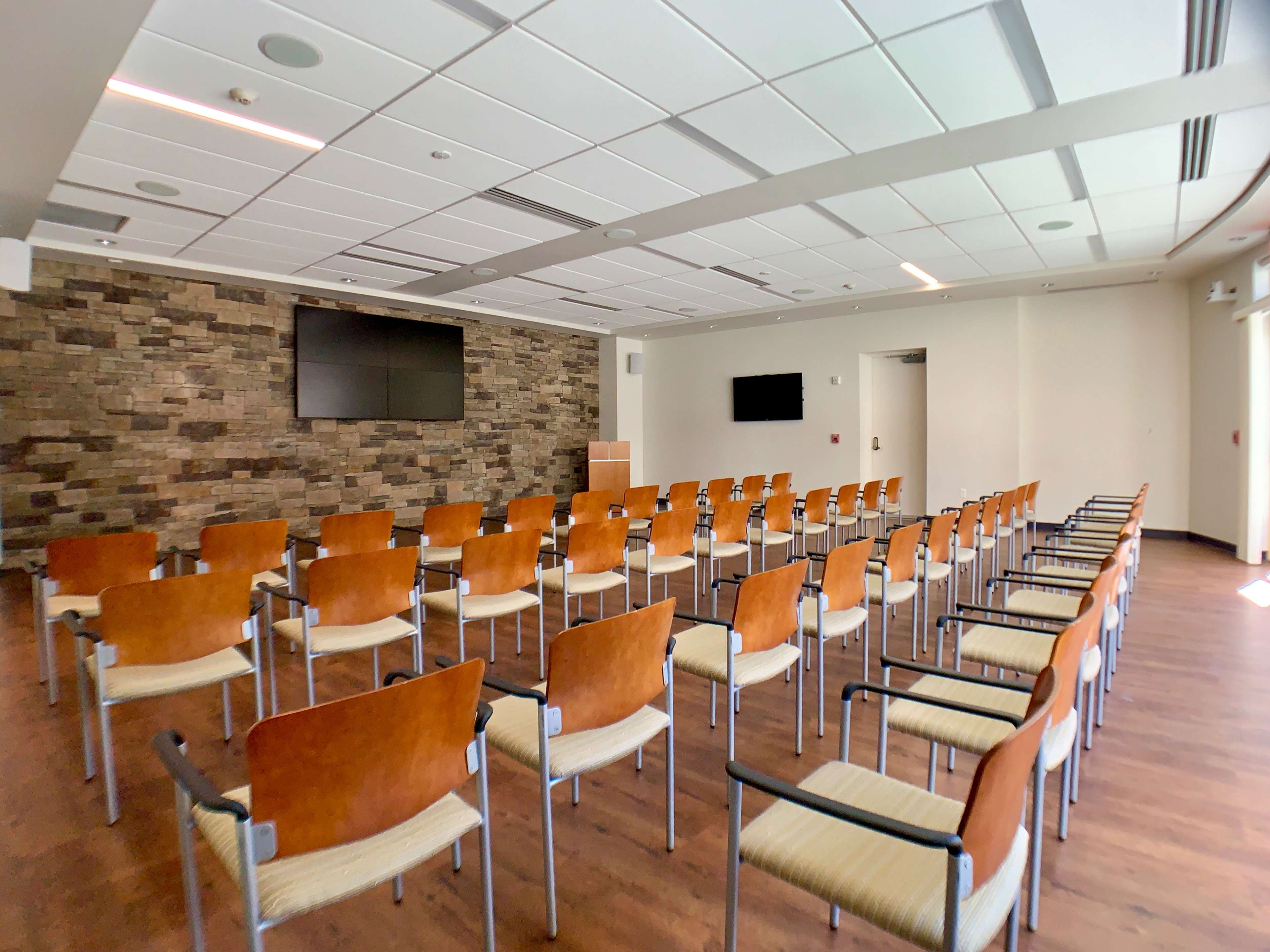 A conference room with rows of chairs arranged facing two large screens on a stone wall.