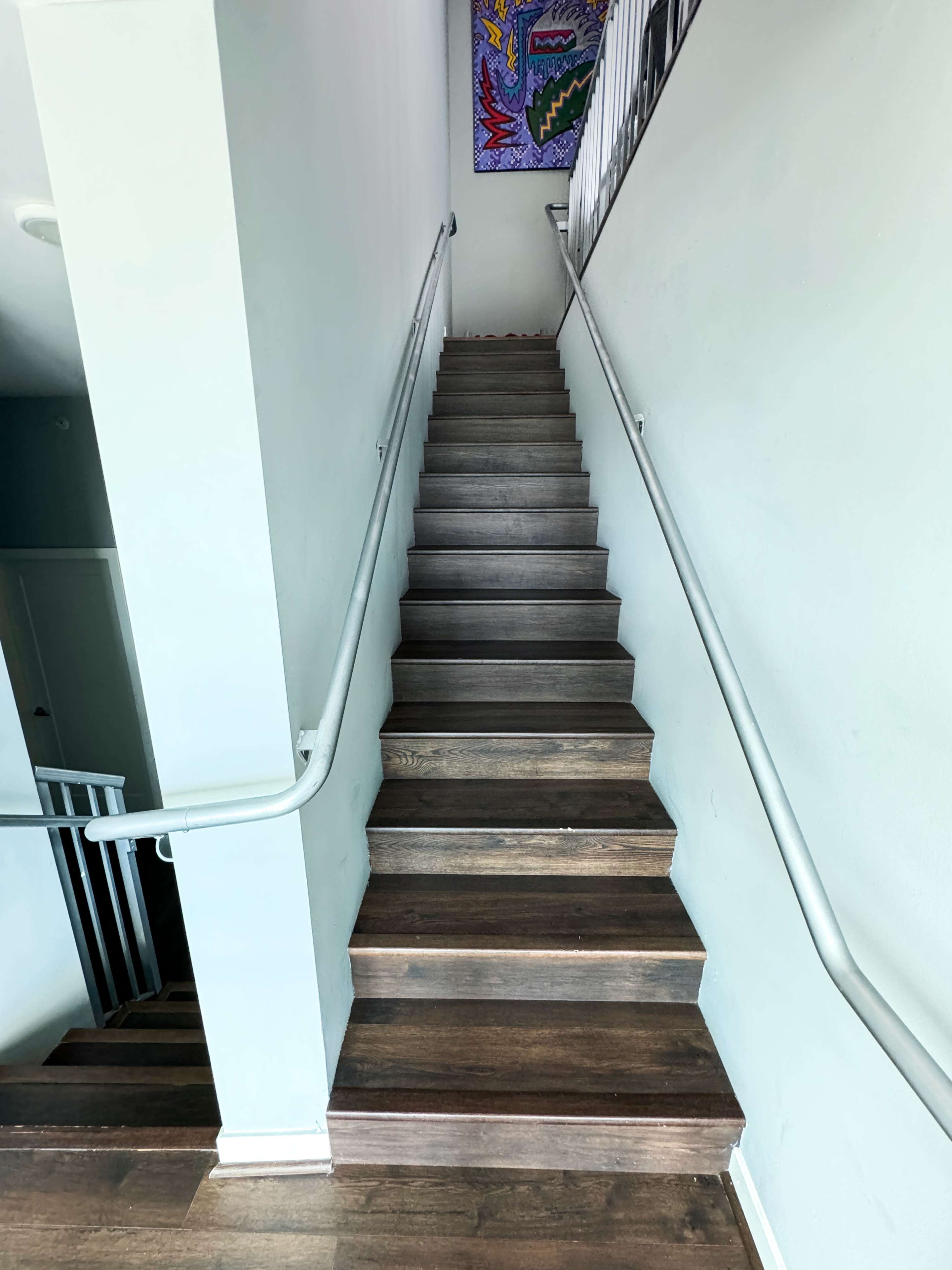 A set of wooden stairs leads upward along a light-colored wall, with a handrail on one side and decorative artwork visible at the top.