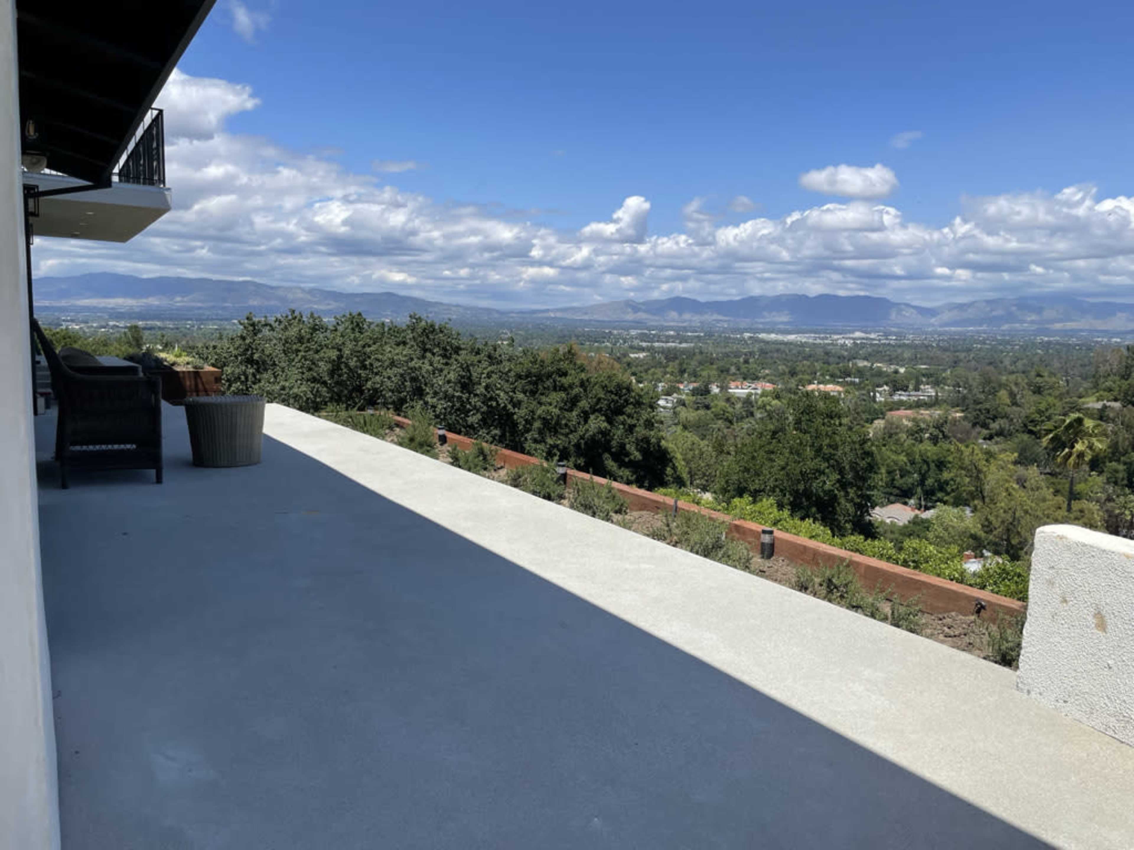 The image shows a concrete patio with a view of a landscape featuring hills, trees, and a cloudy sky.