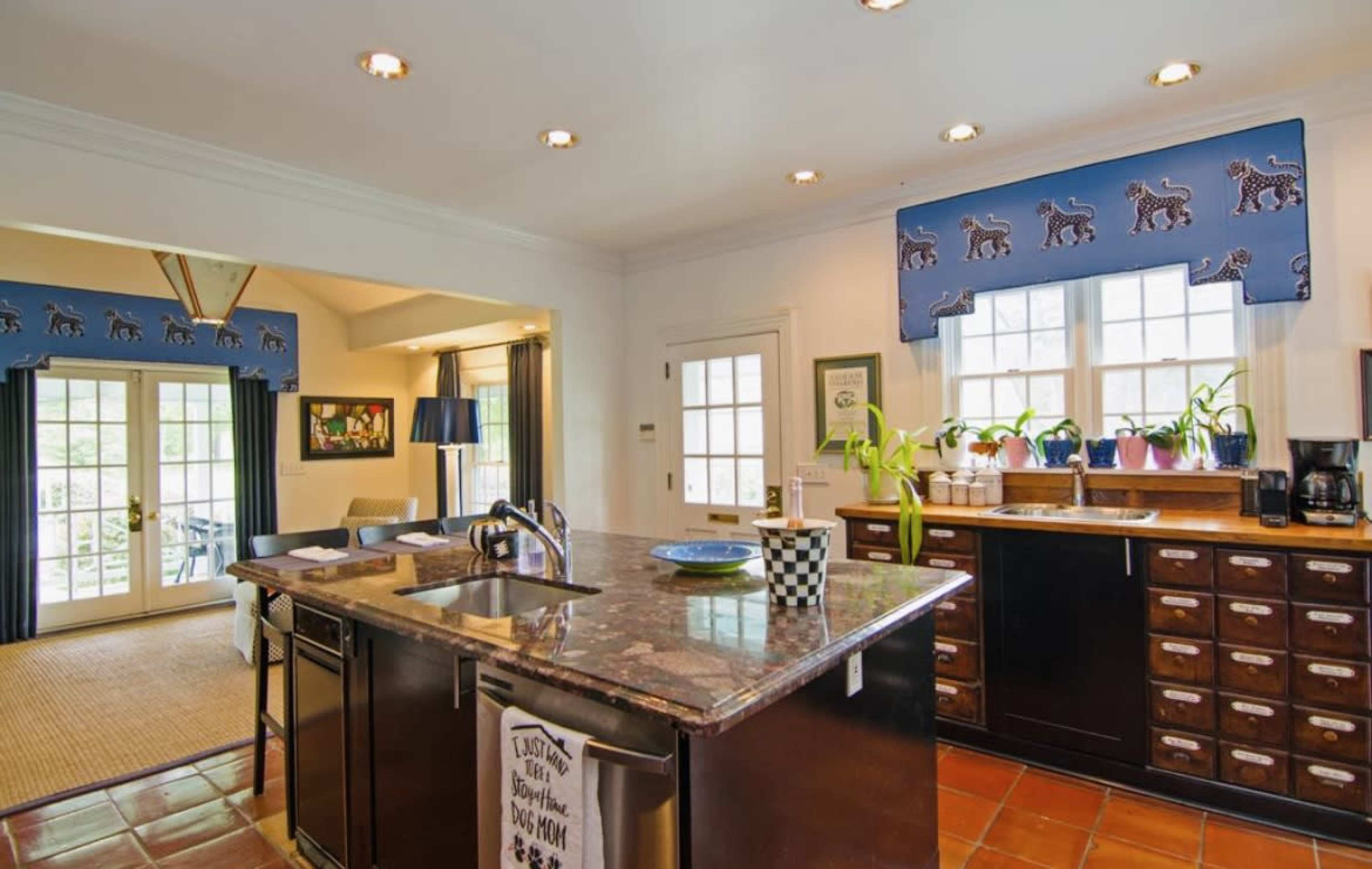 A kitchen with dark wooden cabinets, marble countertops, and a view of an adjacent living area with large windows and sliding doors.