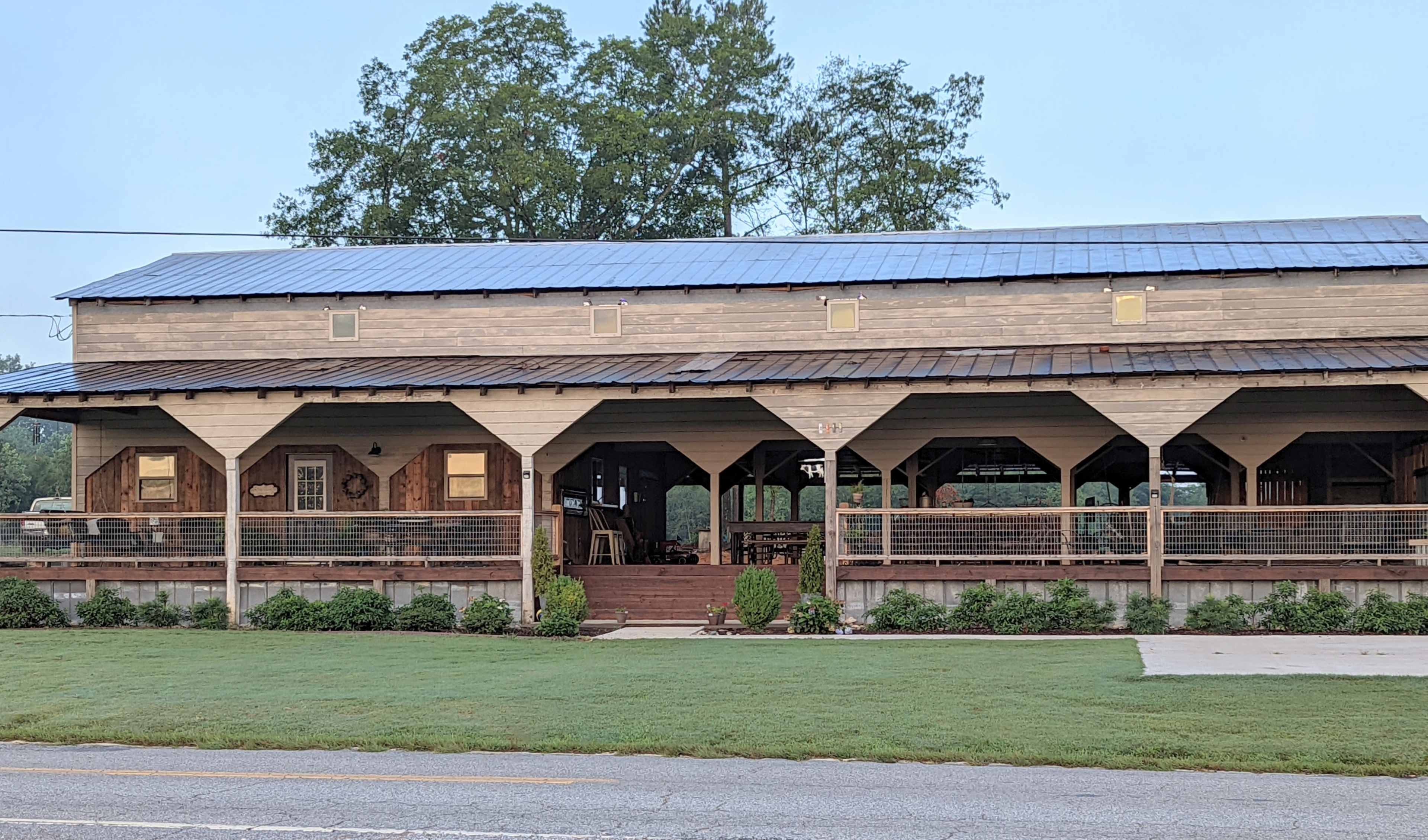 A two-story wooden building with a covered porch and large windows, set against a backdrop of trees and grass.
