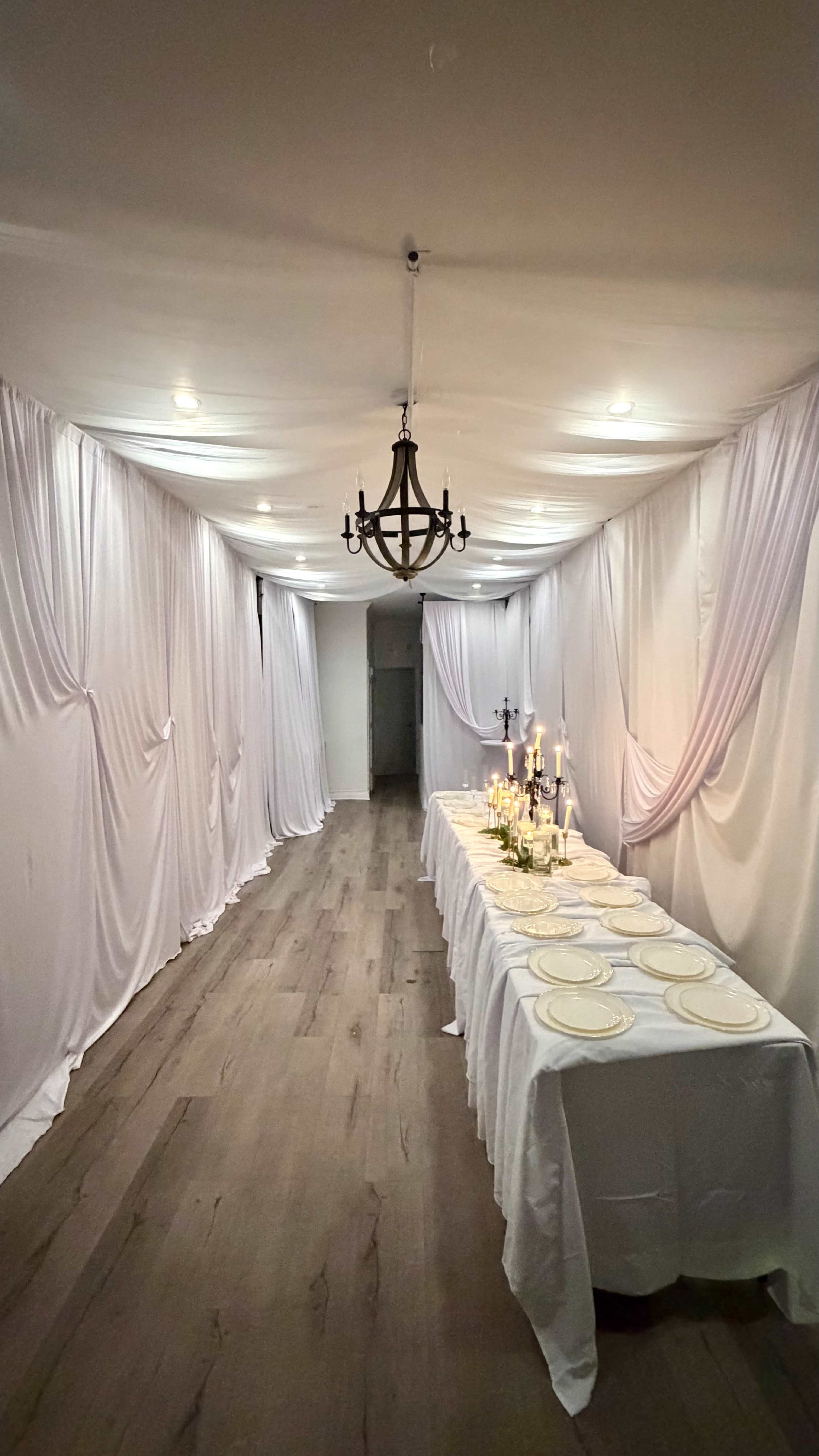 A hallway is decorated with draped white fabric and features a table set with plates and candles.