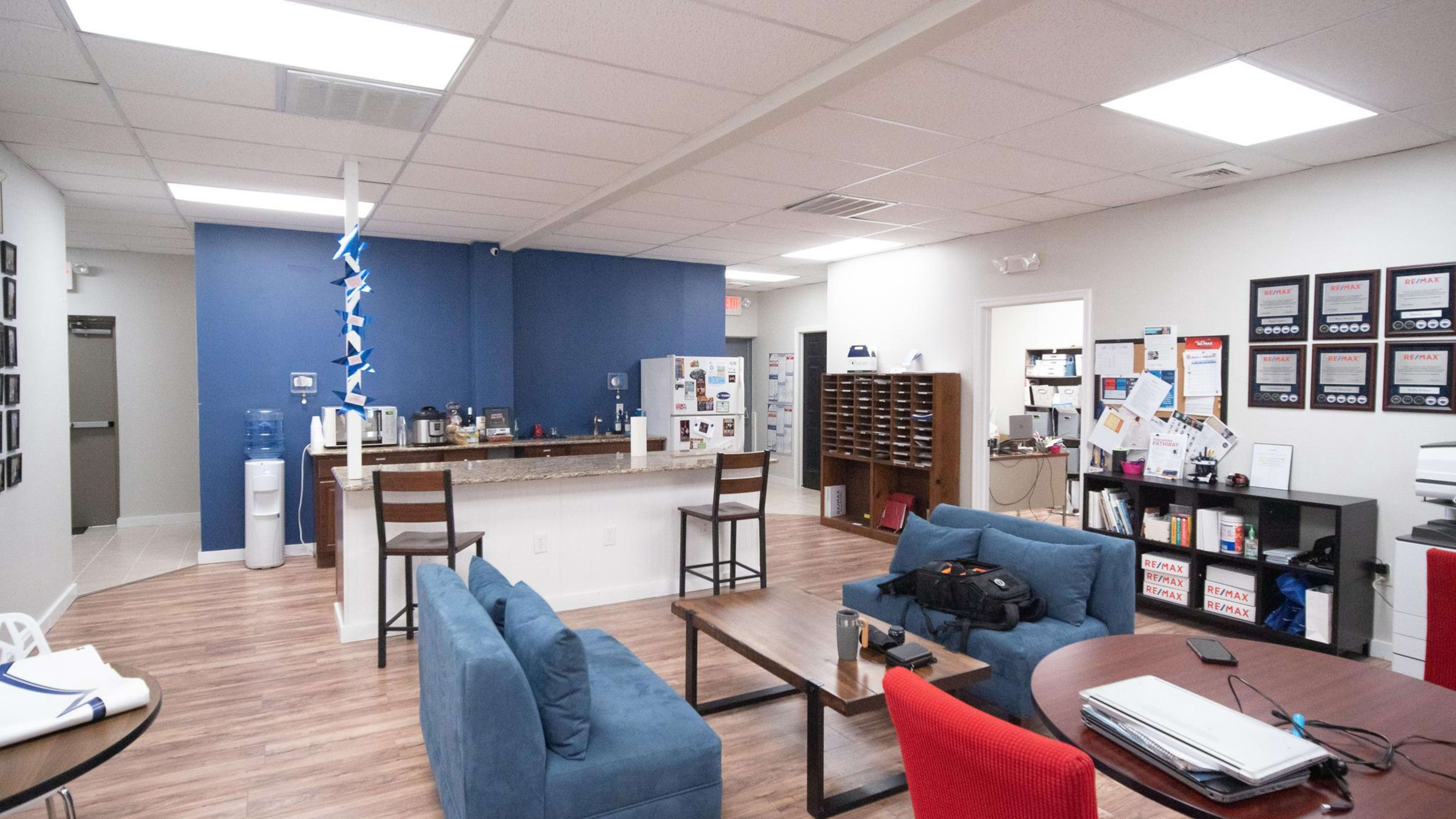A modern break room featuring a lounge area with blue sofas, a kitchenette with bar stools, and a wall of mail slots.