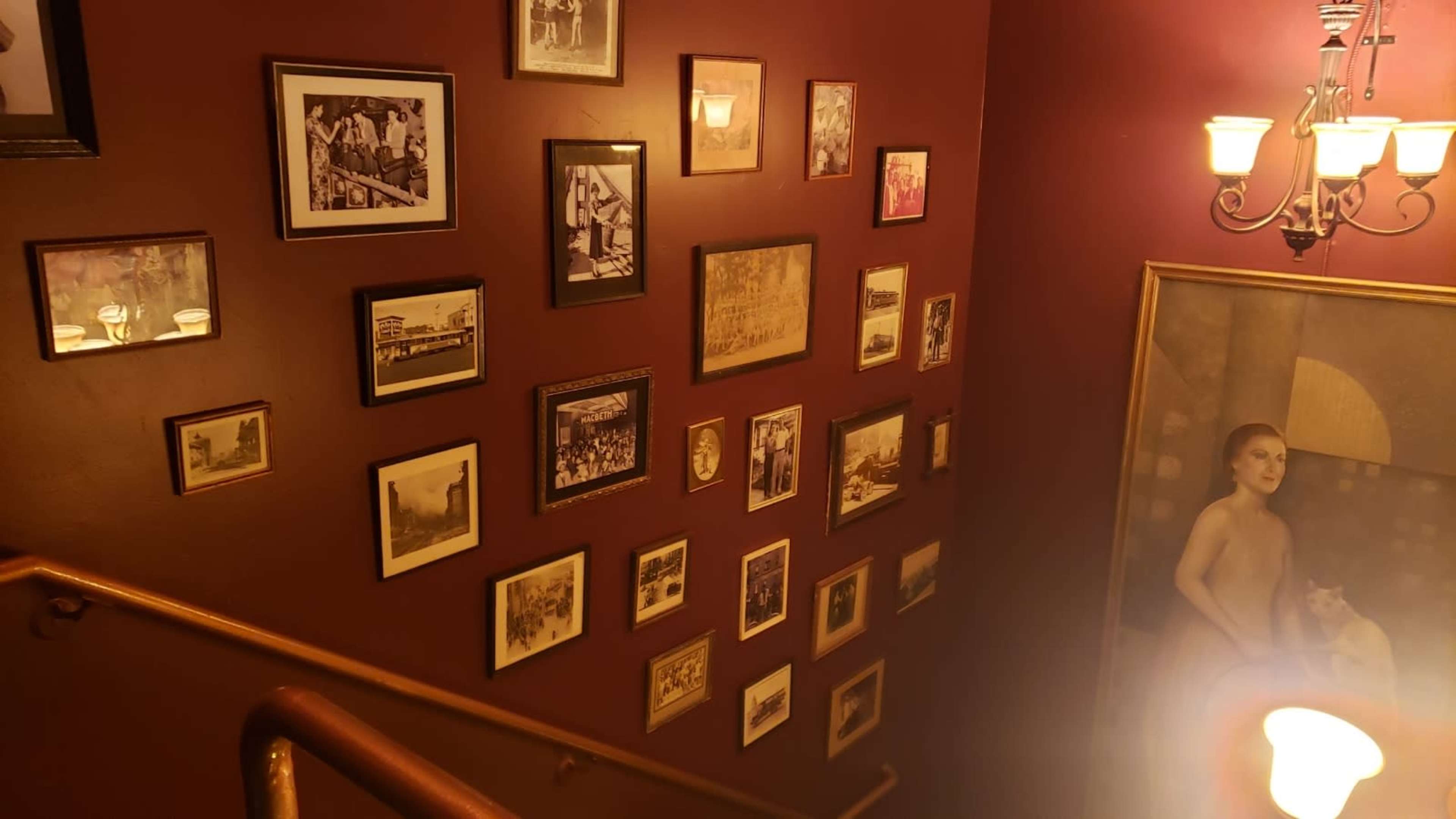 A staircase with a wall adorned with a variety of framed photographs and artwork, illuminated by a nearby chandelier.