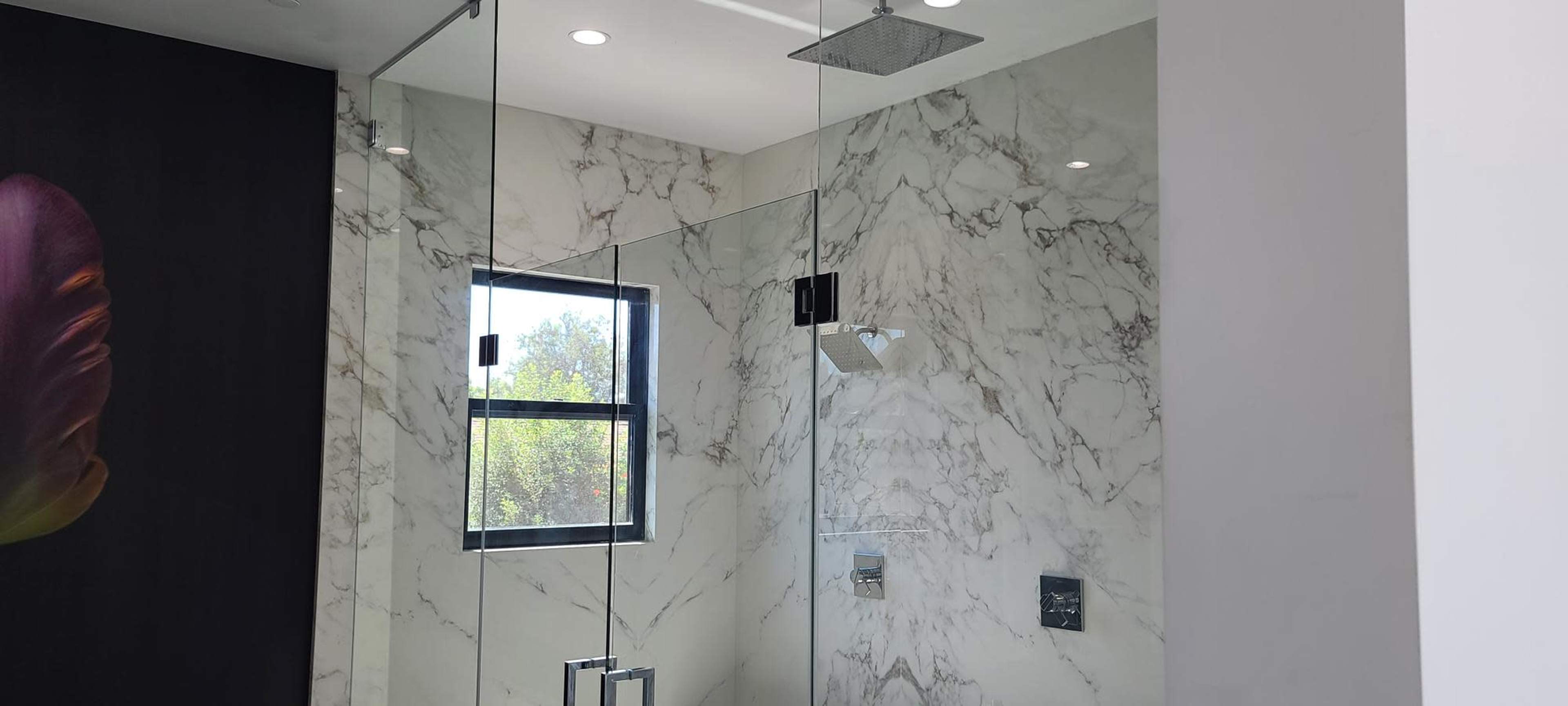 A modern glass shower enclosed by marble walls with a window and overhead rainfall showerhead.