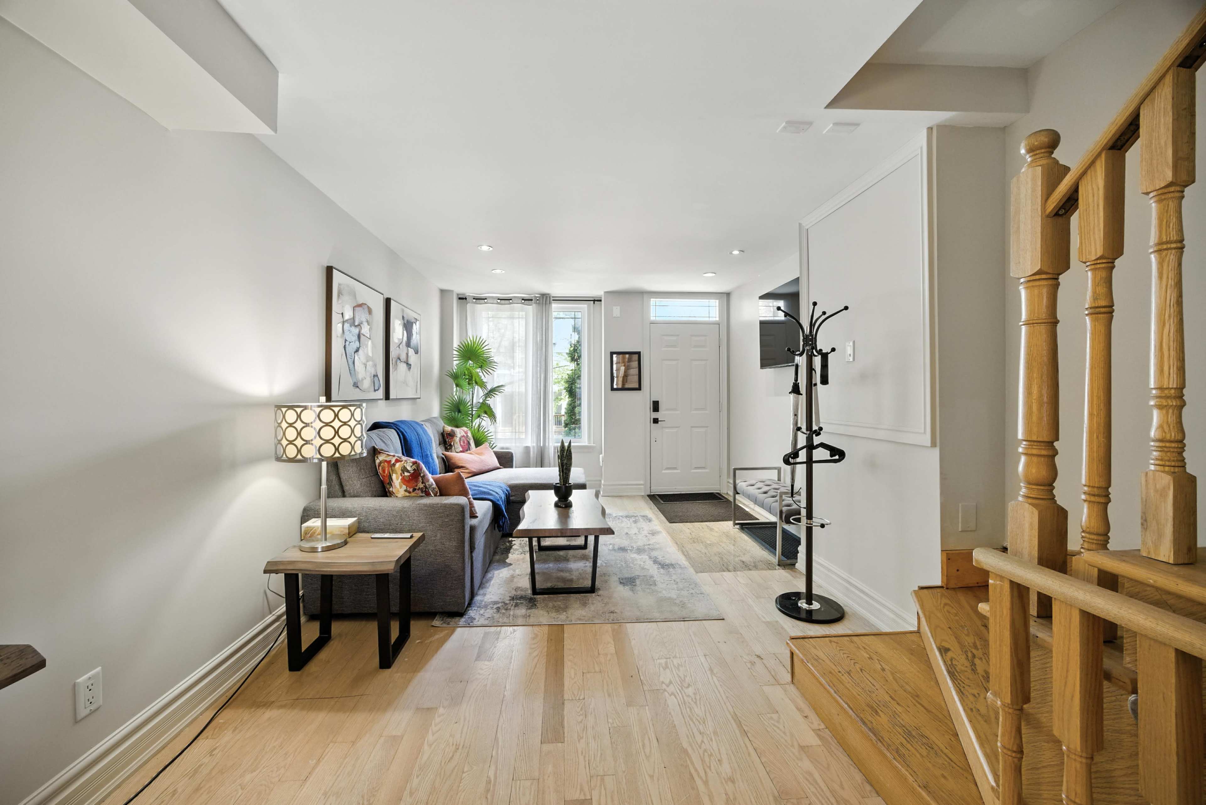 The image shows a modern living room with a sofa, coffee table, and a front door leading to a hallway and staircase.