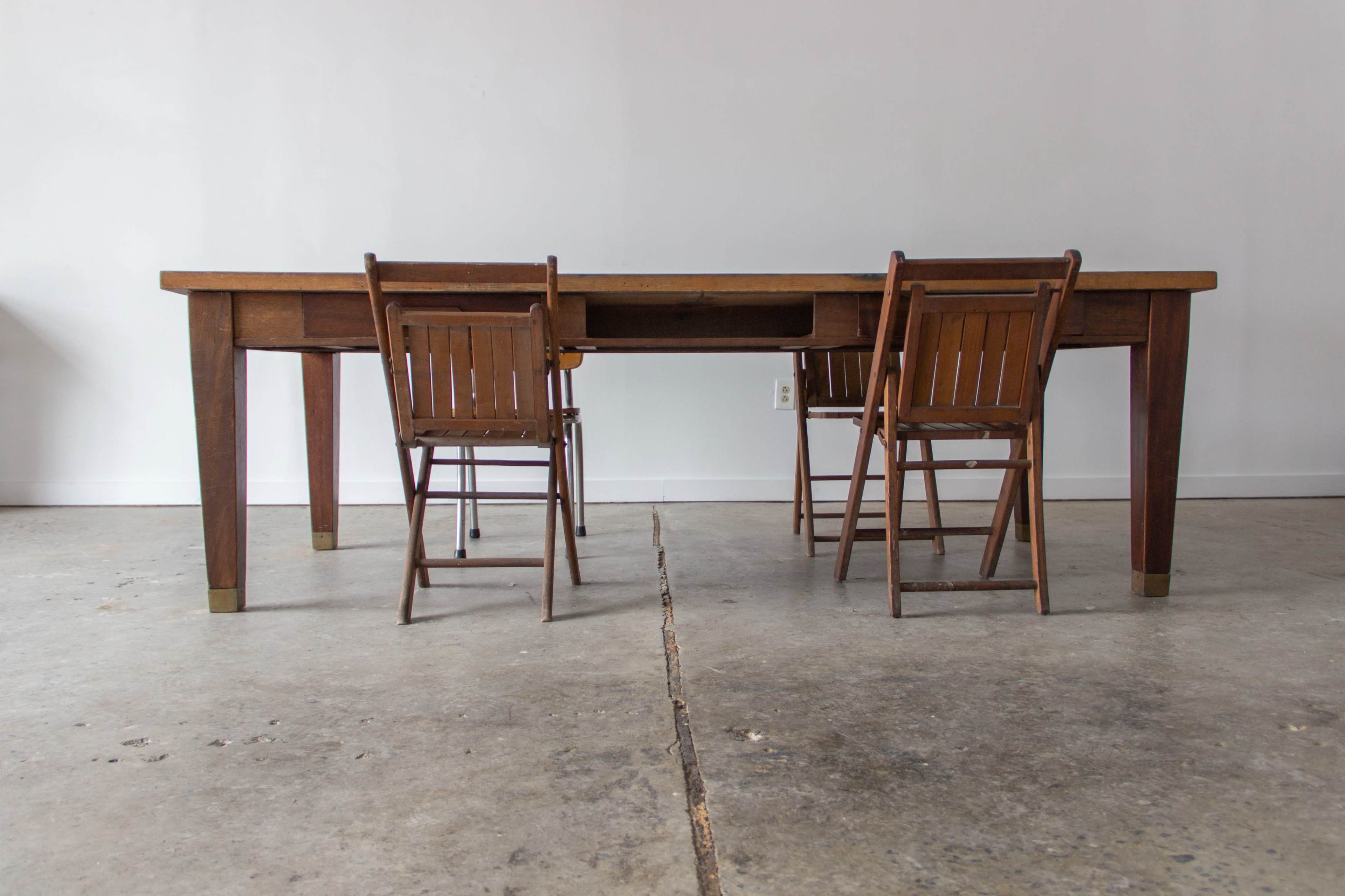 A wooden table with a central drawer is surrounded by two folding chairs on a concrete floor in a minimalist room.