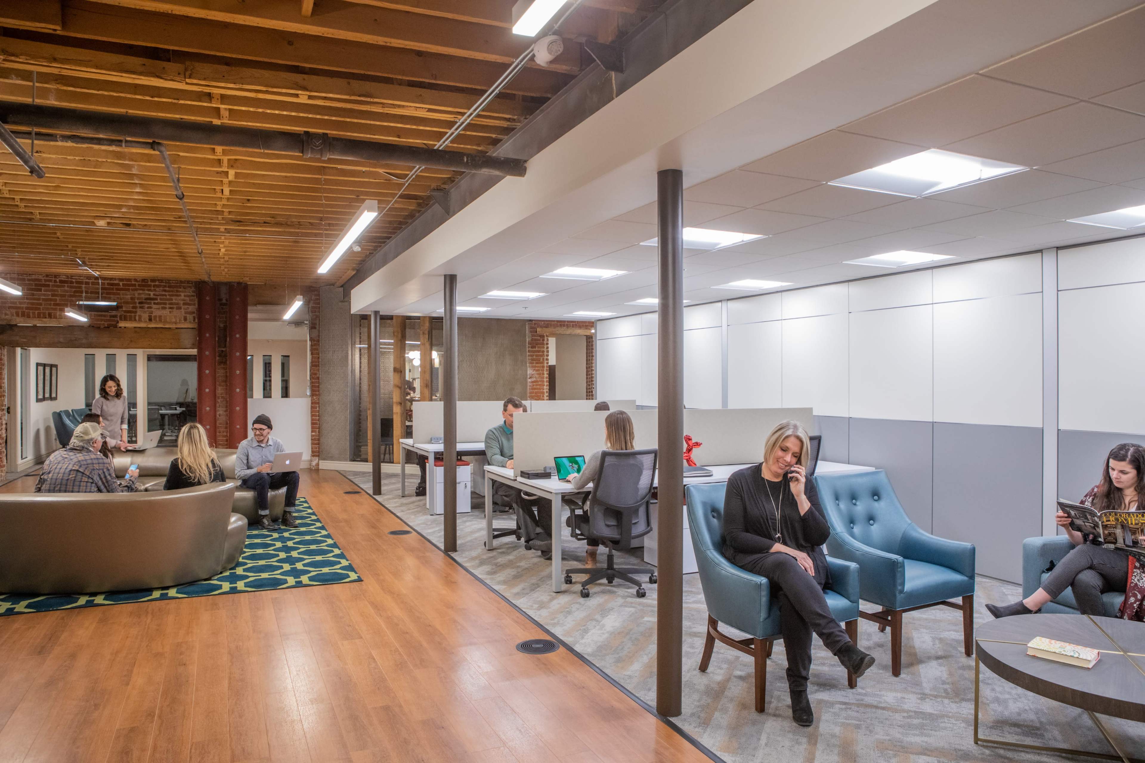 A modern office space with a mix of collaborative areas, individual workstations, and lounge seating, featuring people engaged in various activities.