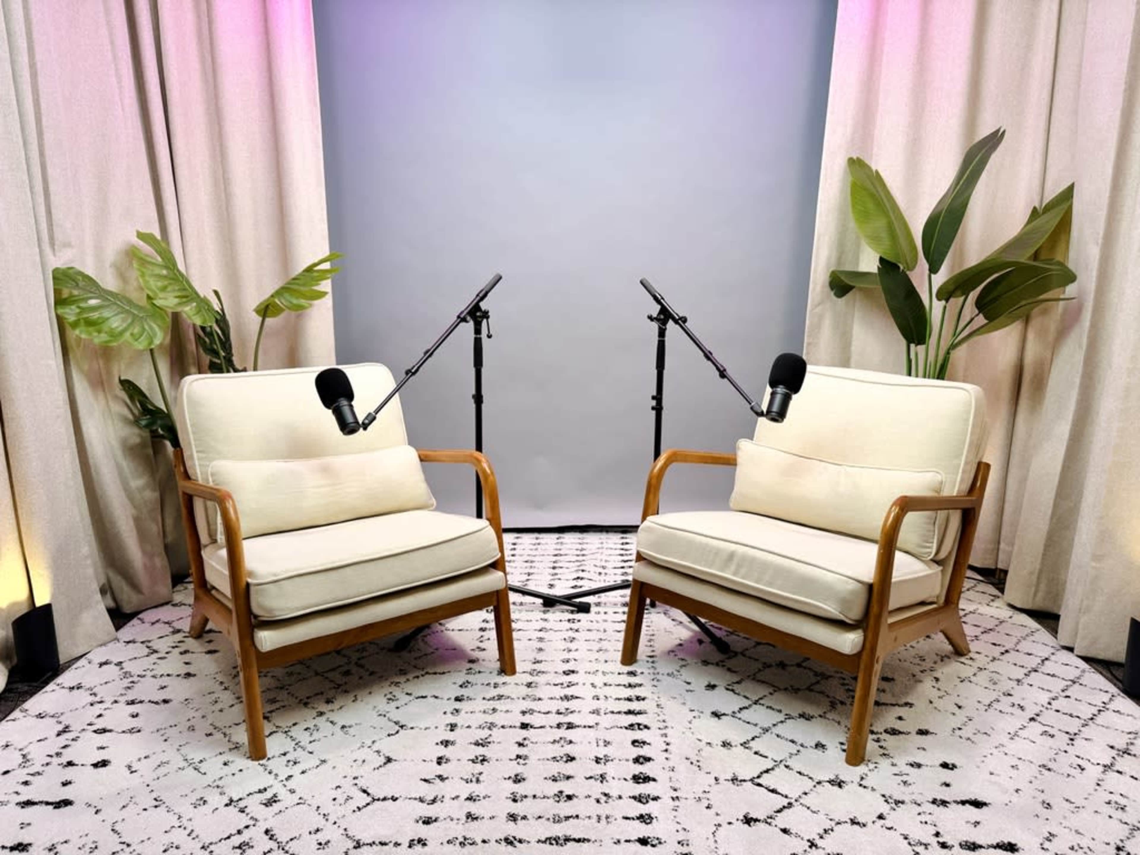 The image shows two chairs with microphones positioned in front of them, surrounded by plants and draped curtains, creating a setting likely intended for an interview or podcast.