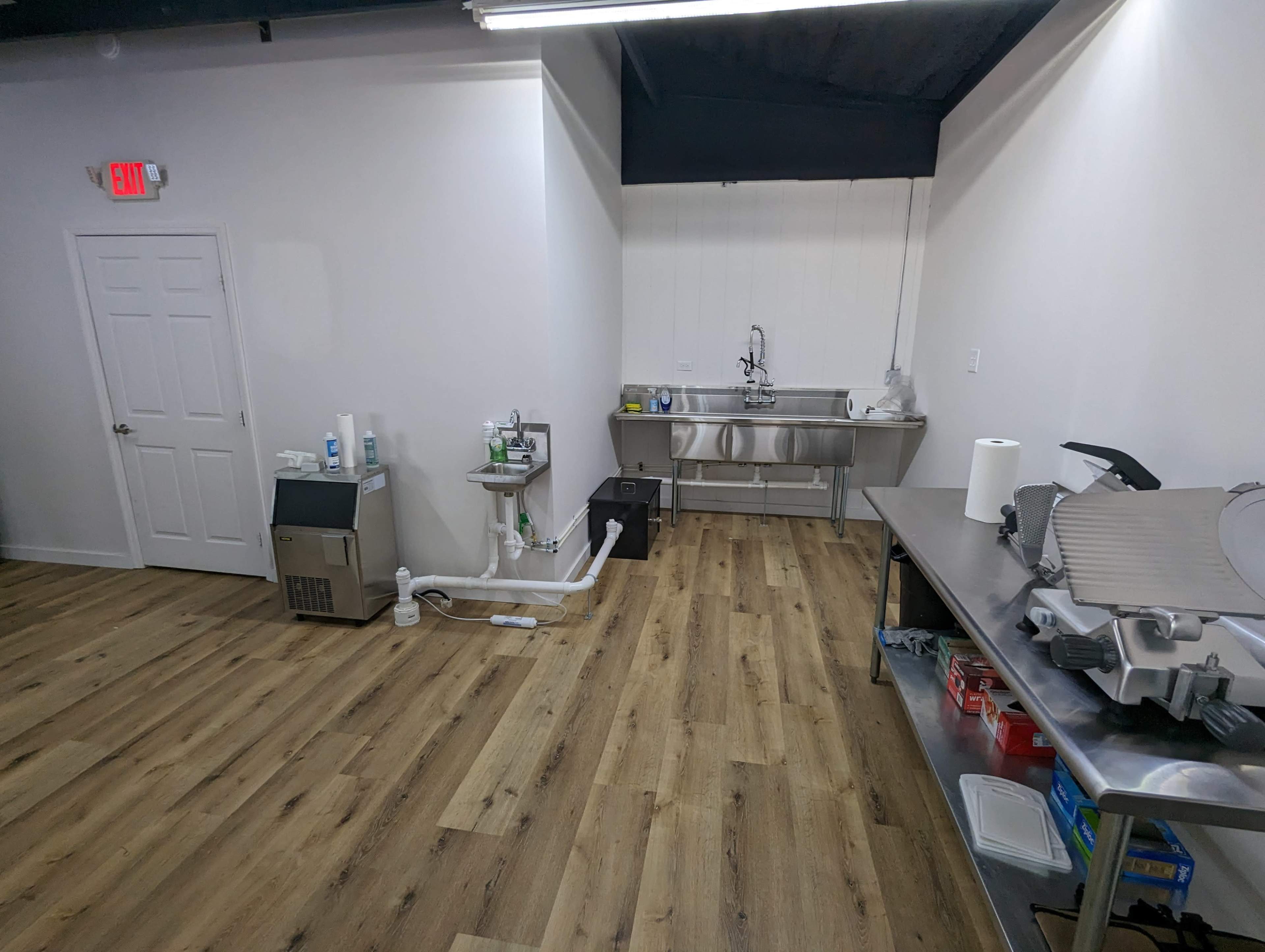 A clean, empty kitchen space featuring stainless steel countertops, sinks, and various kitchen equipment along the walls.