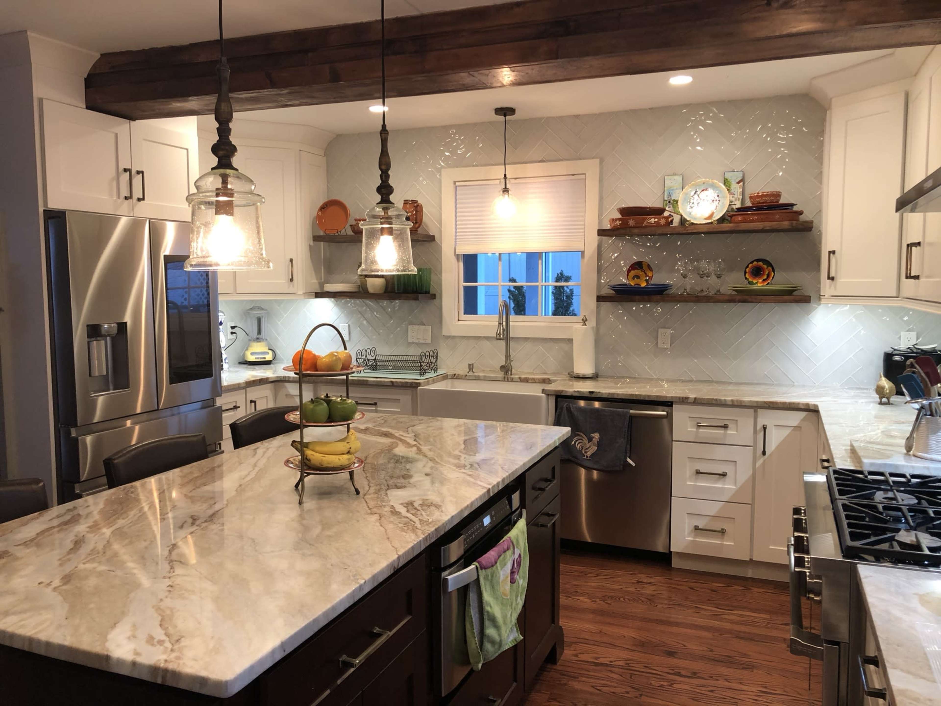 The kitchen features white cabinetry, a marble countertop island with a fruit basket, and pendant lighting over the workspace.