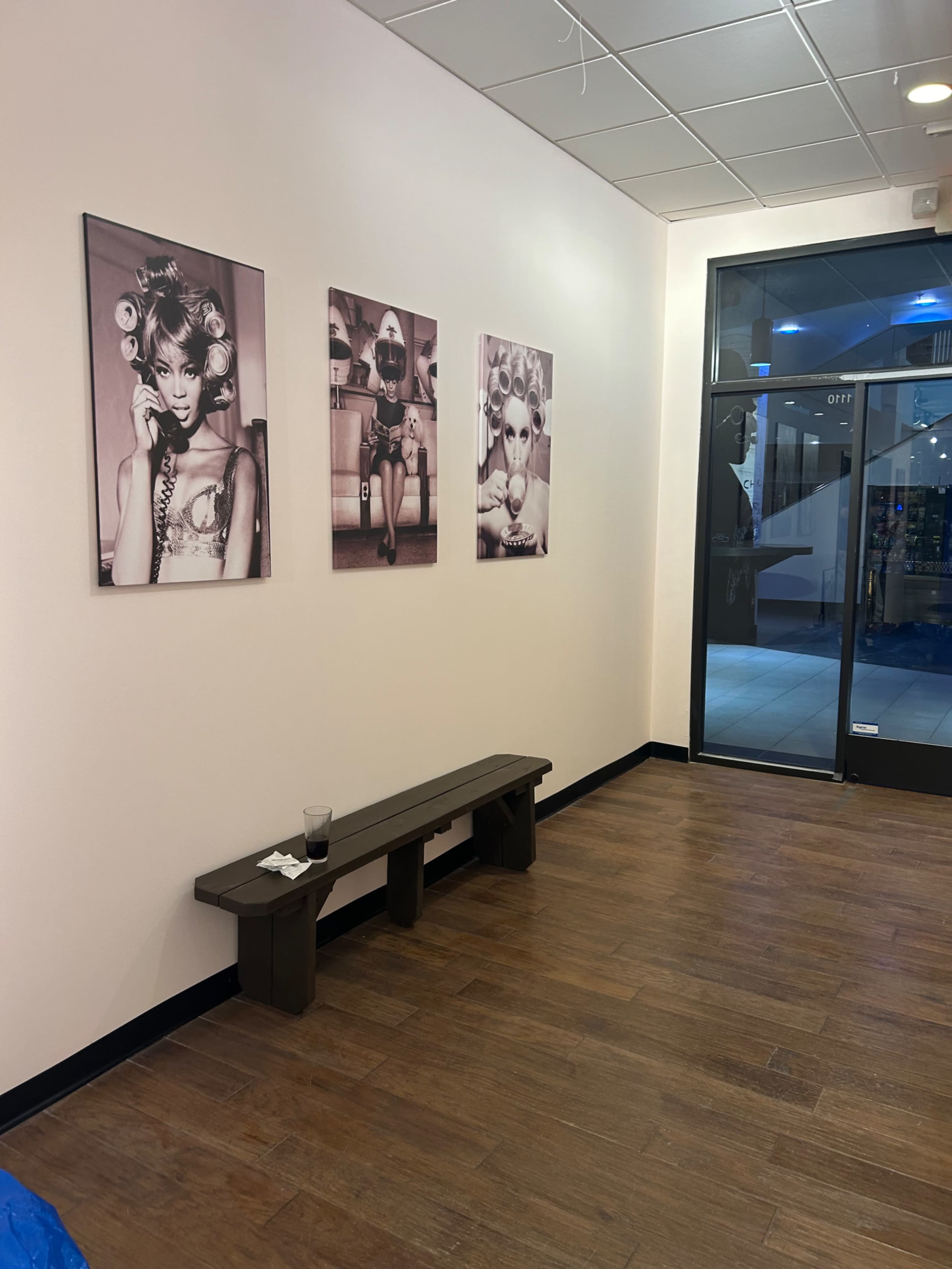 The image shows a vacant interior of a salon or boutique with a wooden bench against the wall and four black-and-white photographs of models displayed on the walls.