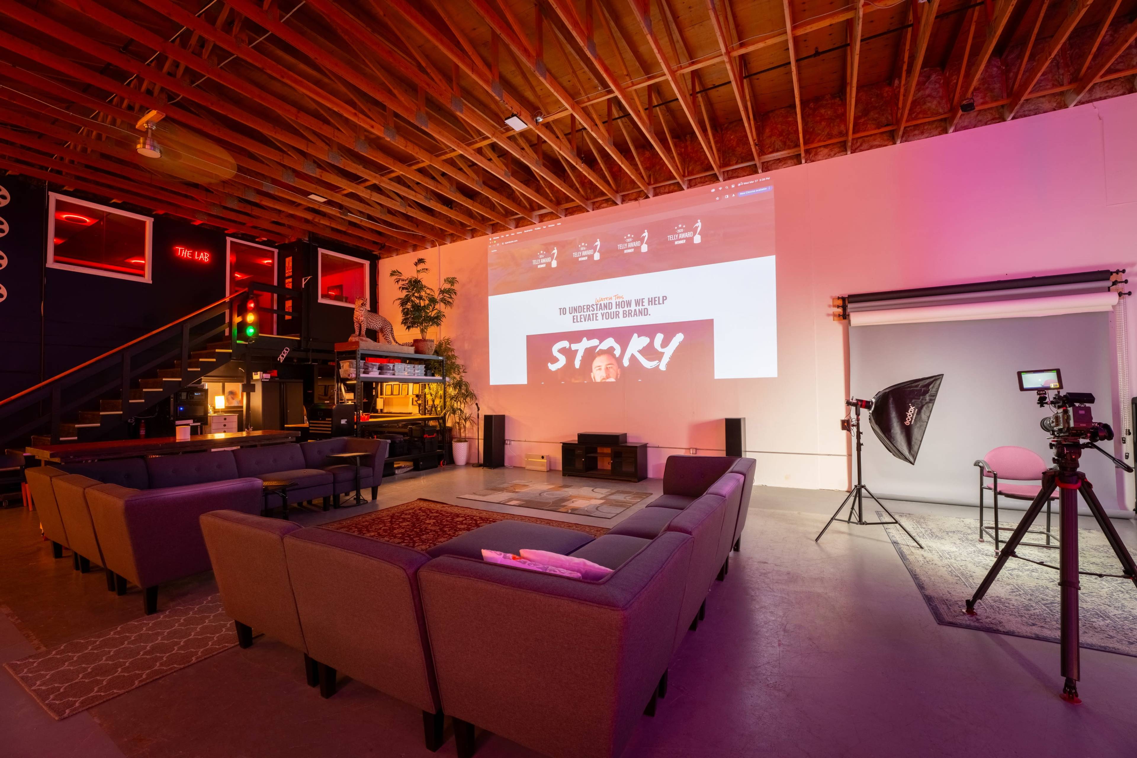 A modern creative space with a seating area, a projector displaying a website, and a photography setup in the corner.