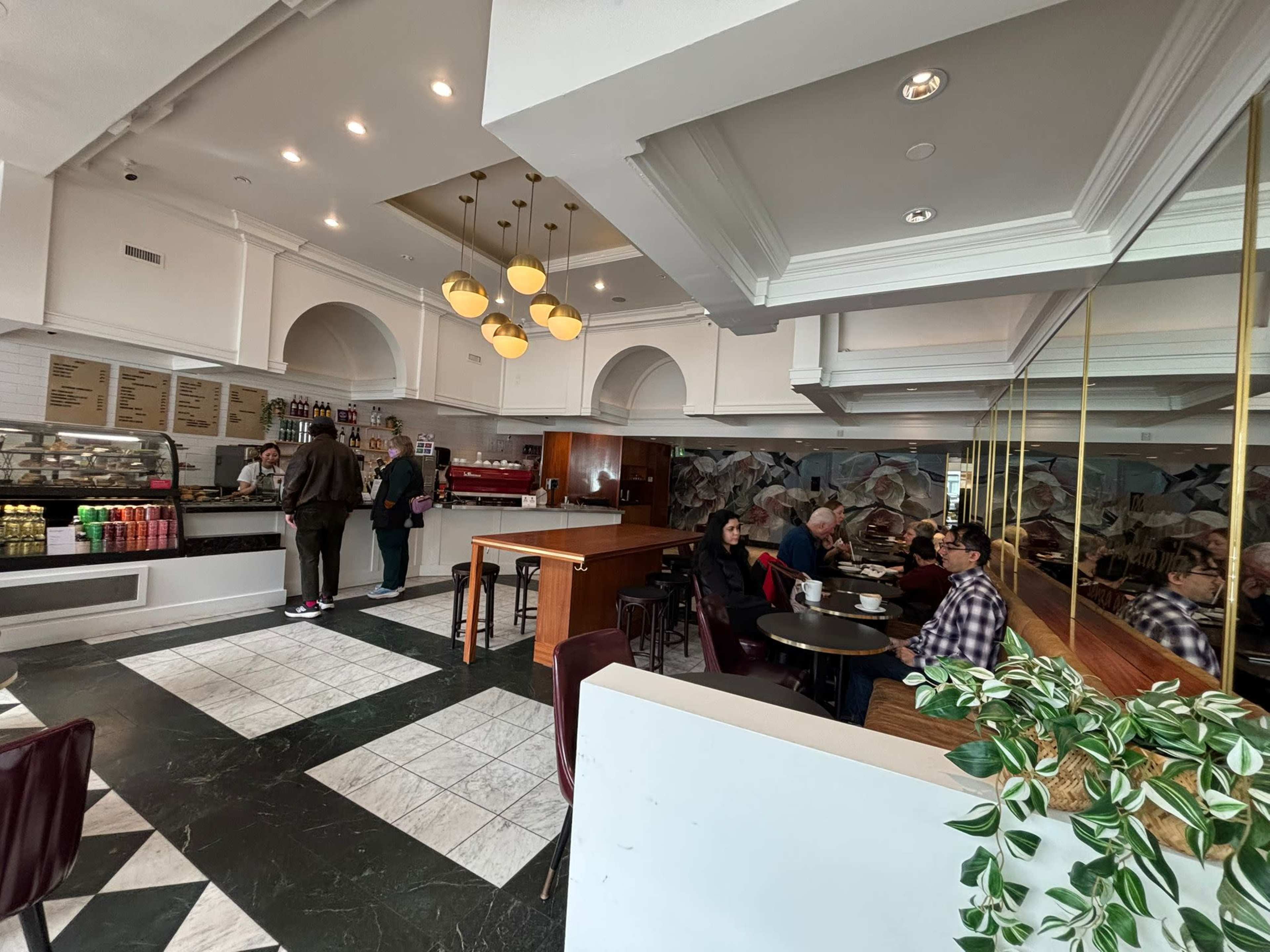 The image shows a modern coffee shop with a seating area and a service counter, where customers are ordering drinks and others are seated at tables.