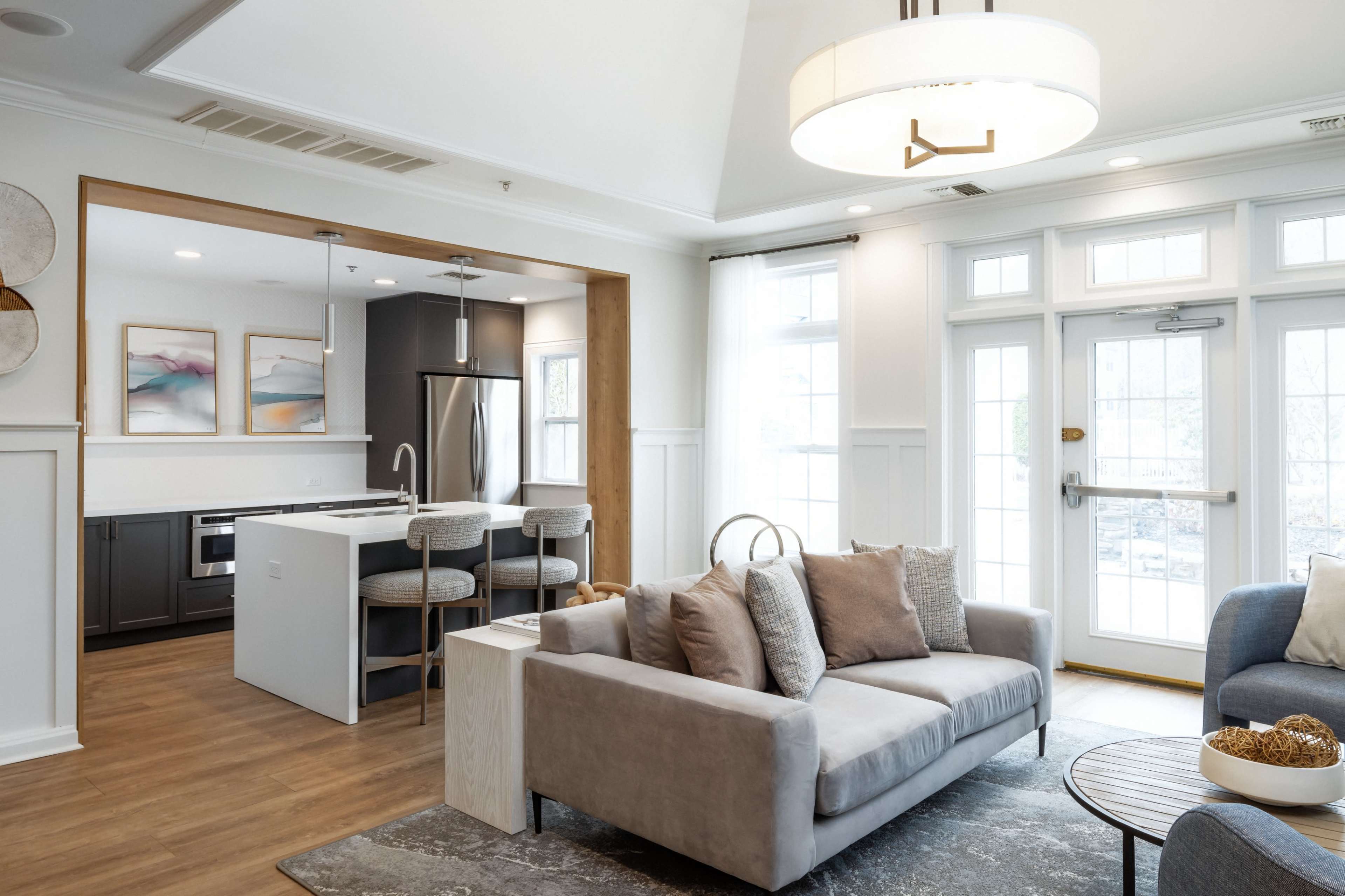 A modern living room with a gray sofa, a small round table, and an adjoining kitchen area featuring a sleek design and stainless steel appliances.