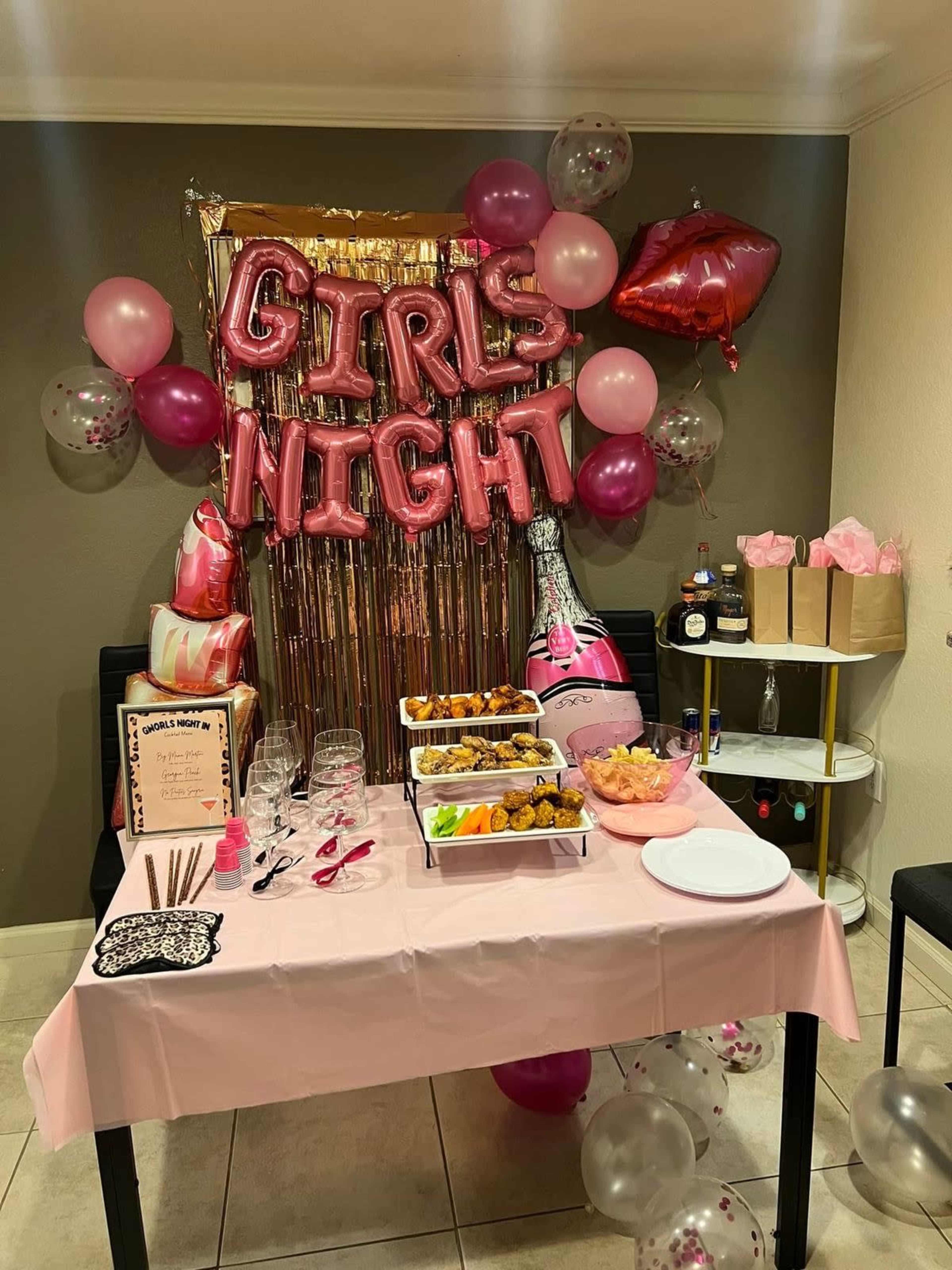 The image depicts a decorated table for a girls' night event, featuring pink balloons, a sparkling backdrop, food platters, and wine glasses.
