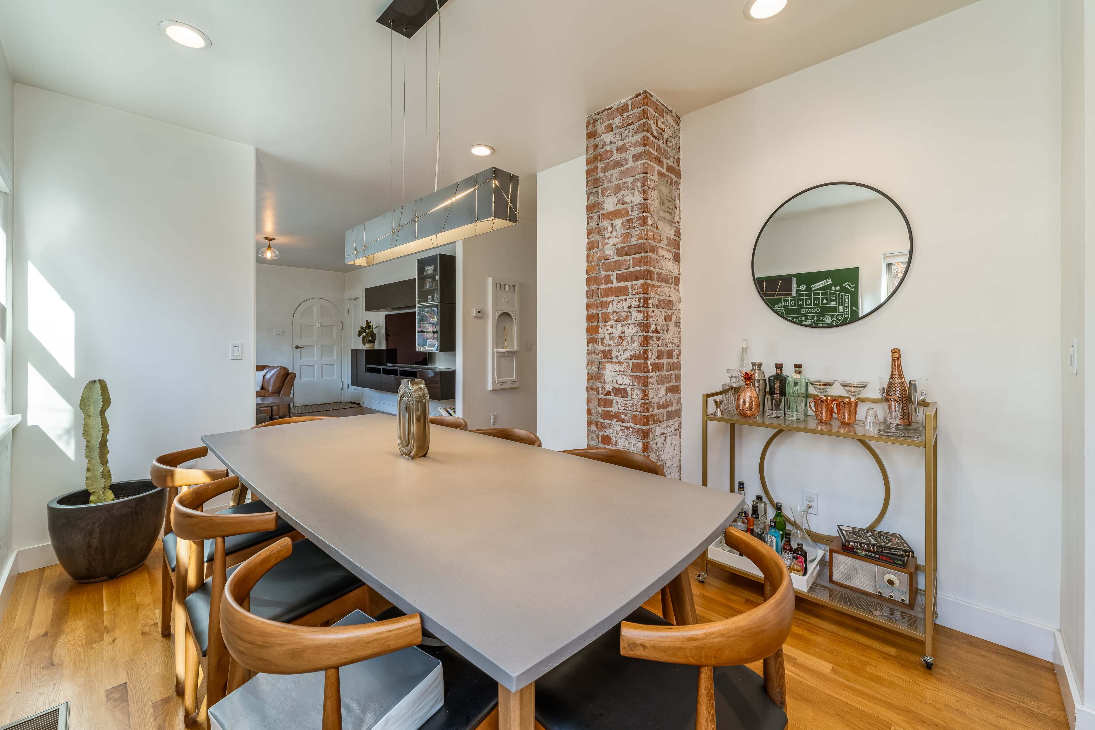 A modern dining area features a sleek table surrounded by wooden chairs, a mirrored wall accent, and a brick column.