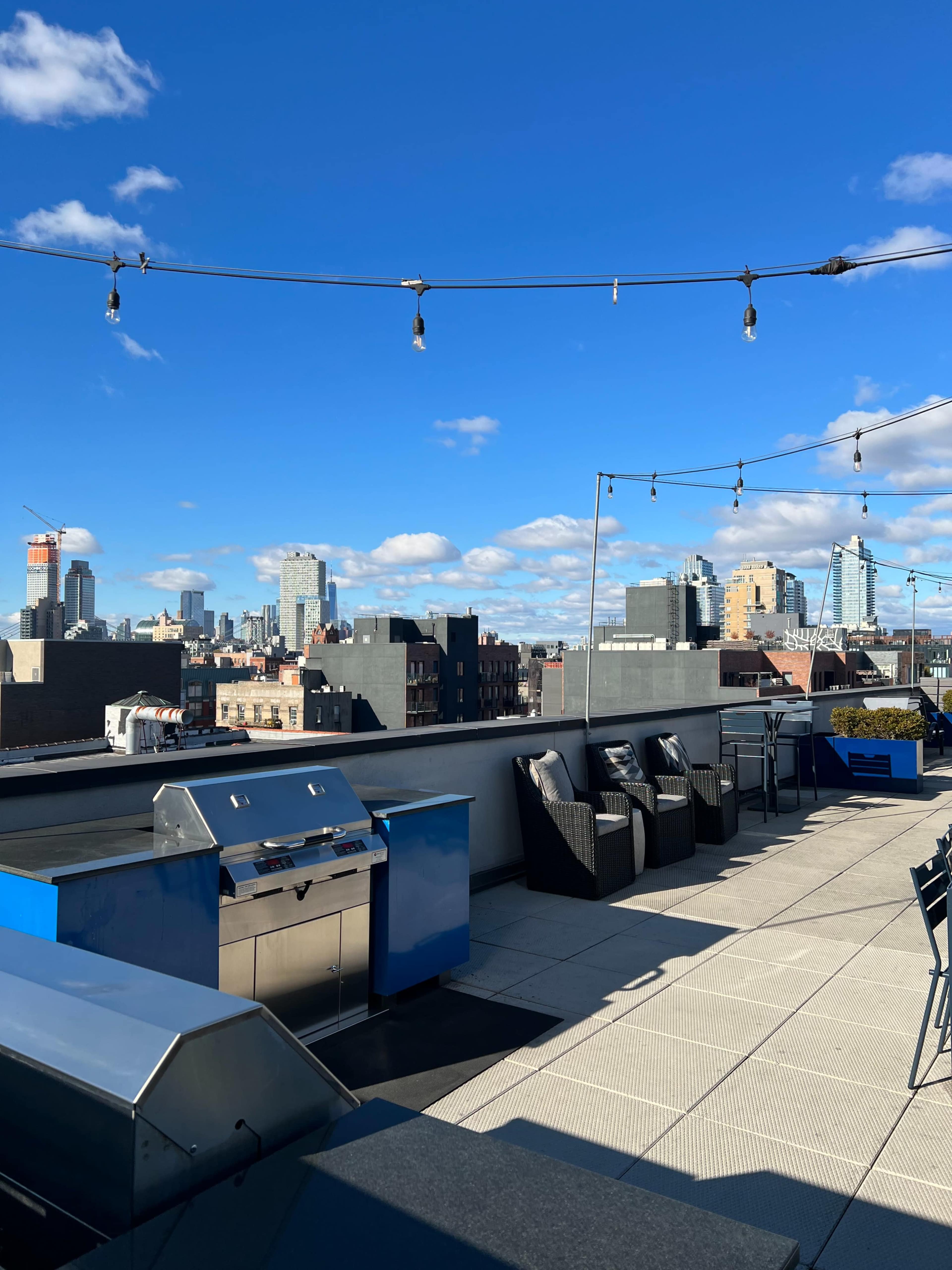 The rooftop area features grills and seating with a view of a skyline under a clear blue sky.