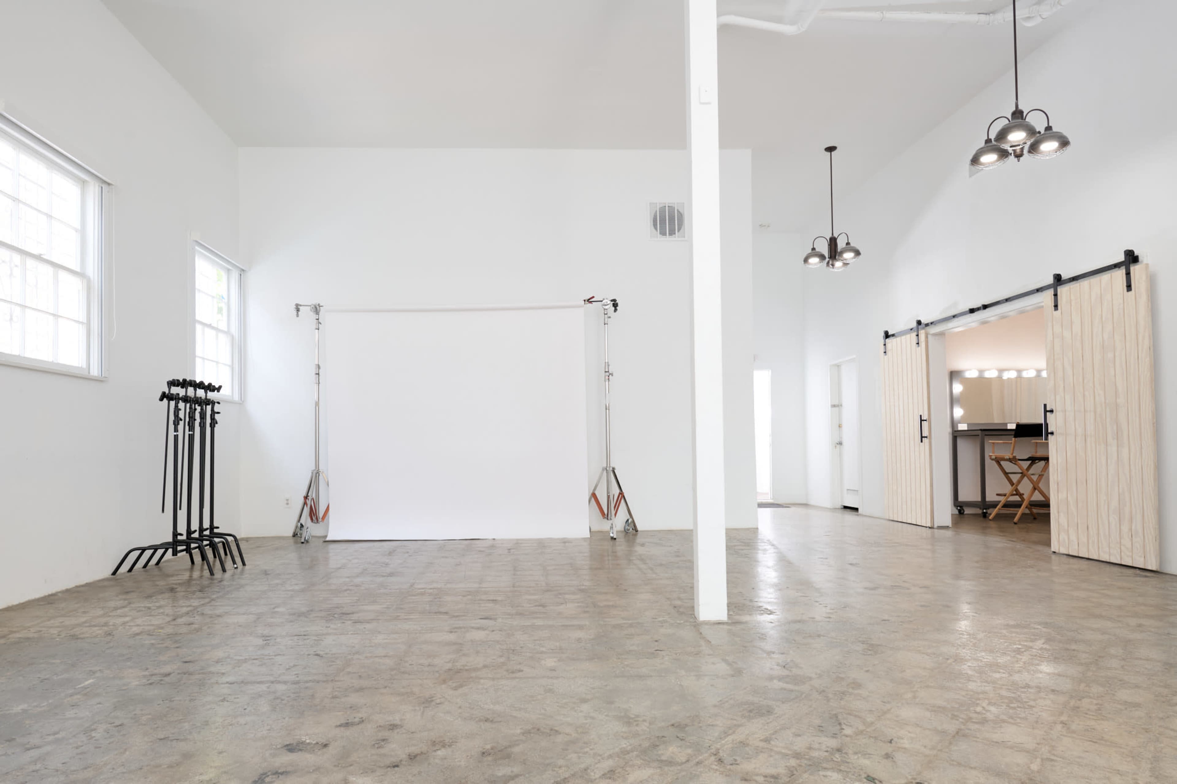 The image shows a spacious, empty room with a white backdrop at one end and a bar-style counter visible through sliding barn doors on the other side.