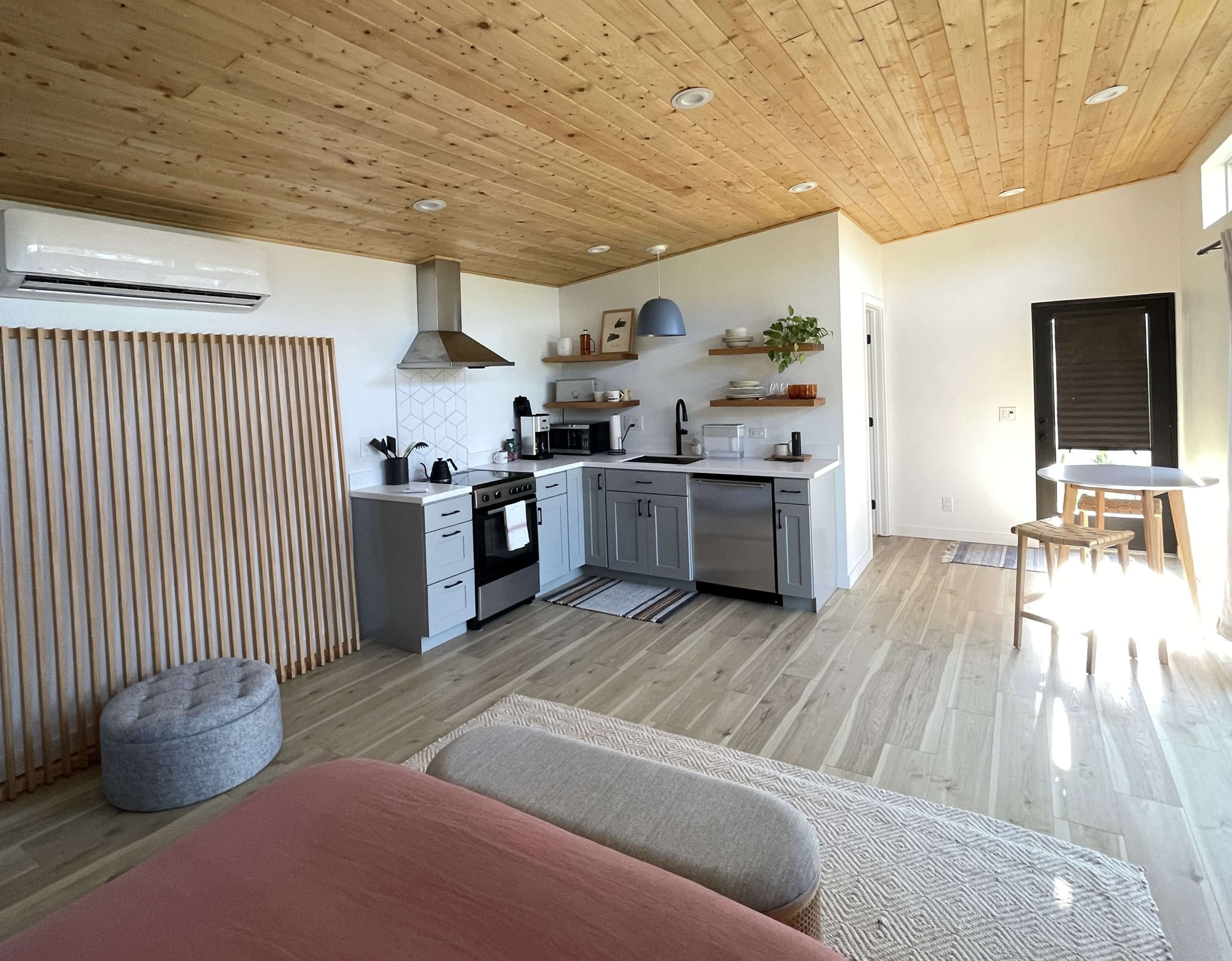 A modern kitchen area featuring gray cabinets, a stainless steel stove, and a wooden ceiling in a well-lit open space.