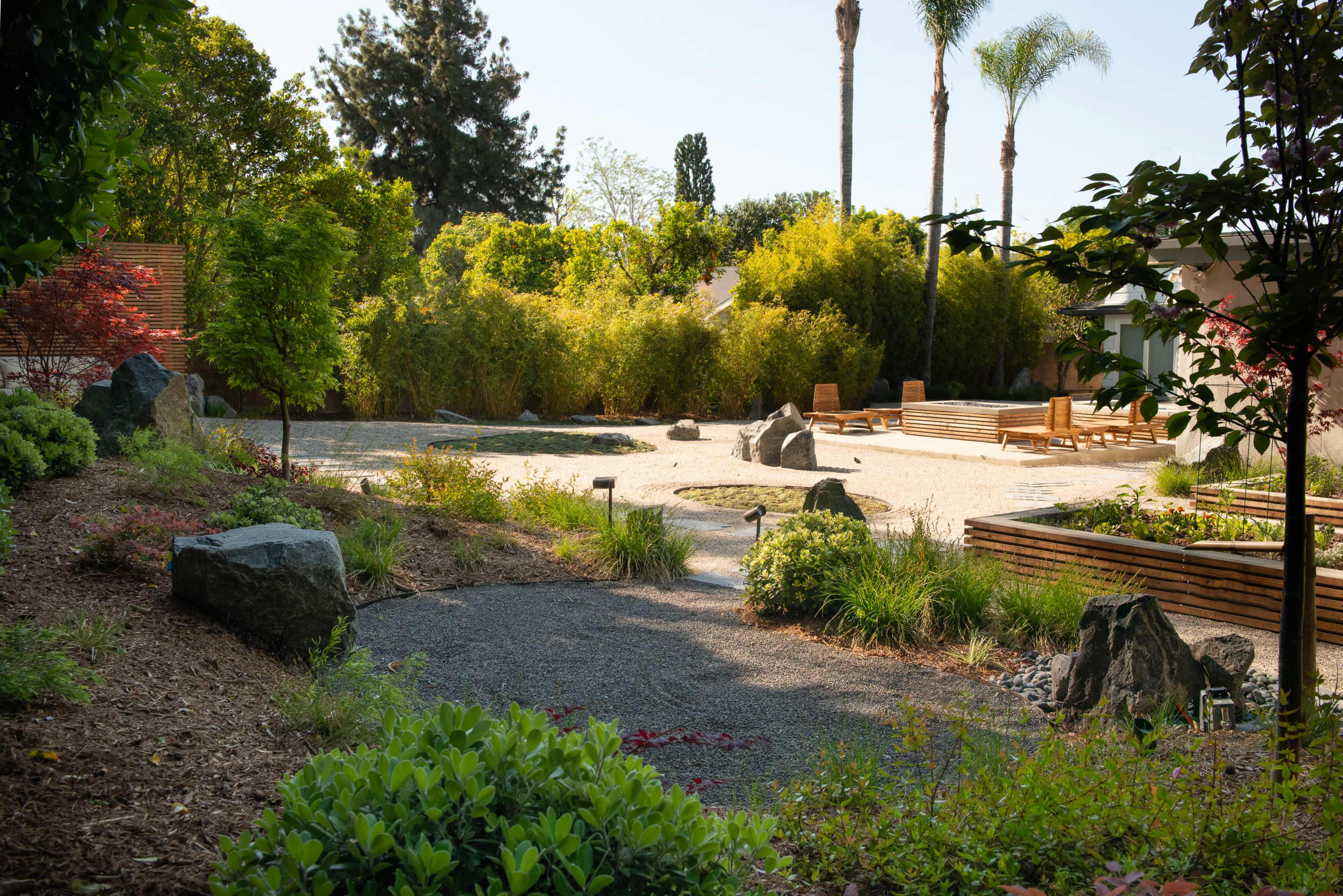 A landscaped garden features gravel paths, rocks, and various plants, with palm trees and bamboo in the background.