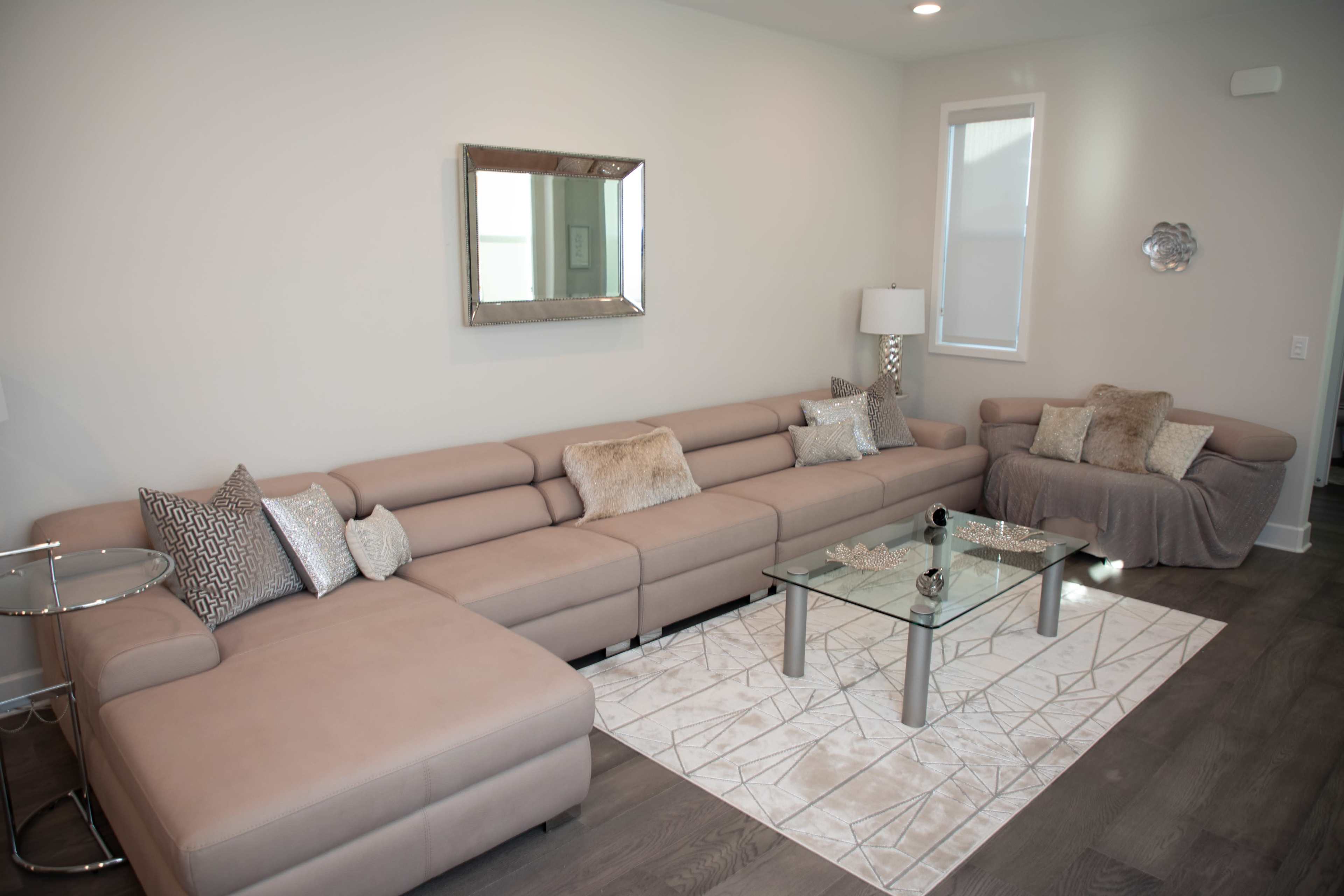 A modern living room featuring a light-colored sectional sofa, a glass coffee table, and a neutral area rug under soft lighting.