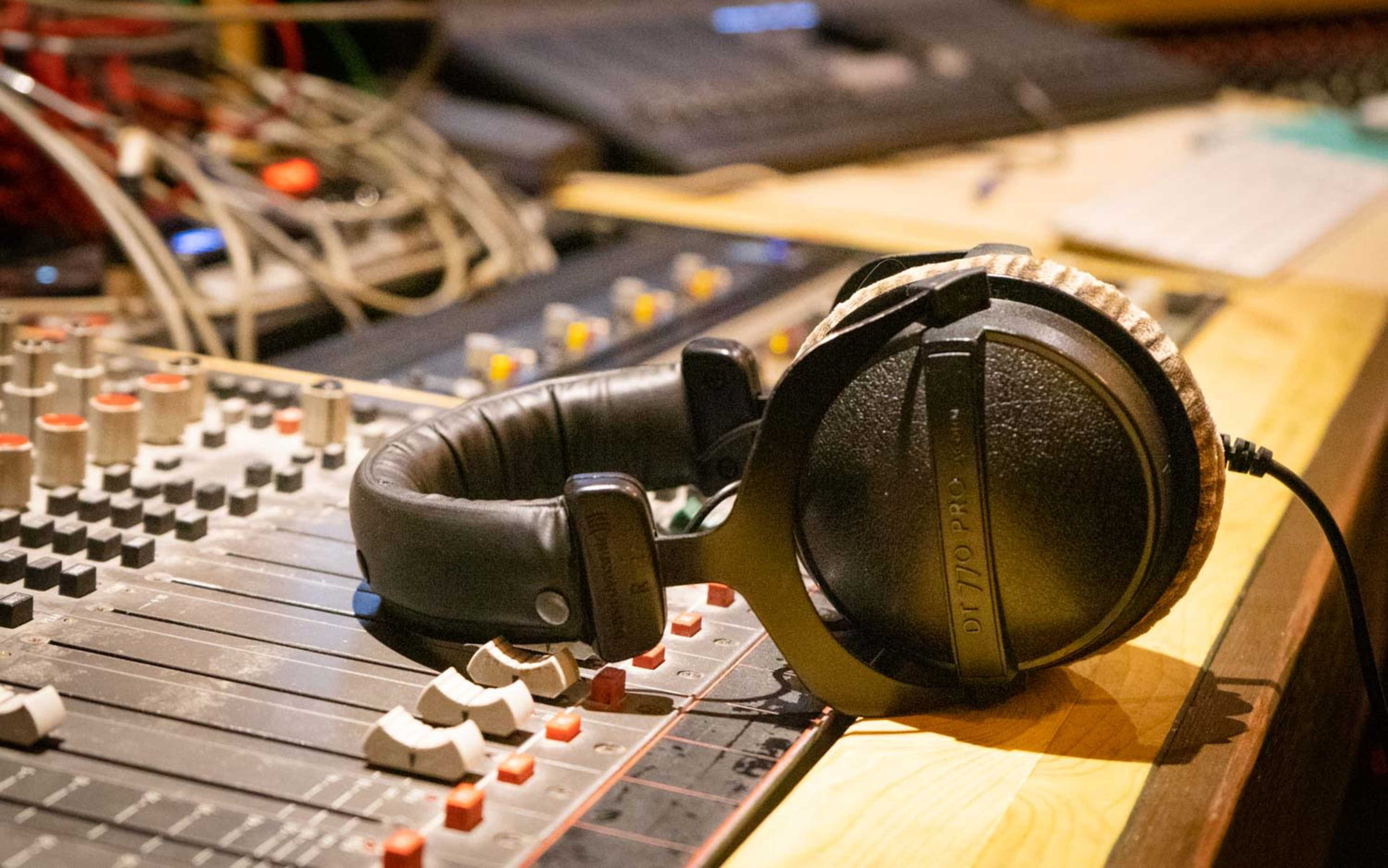 A pair of headphones rests on a sound mixing console surrounded by various cables and equipment.