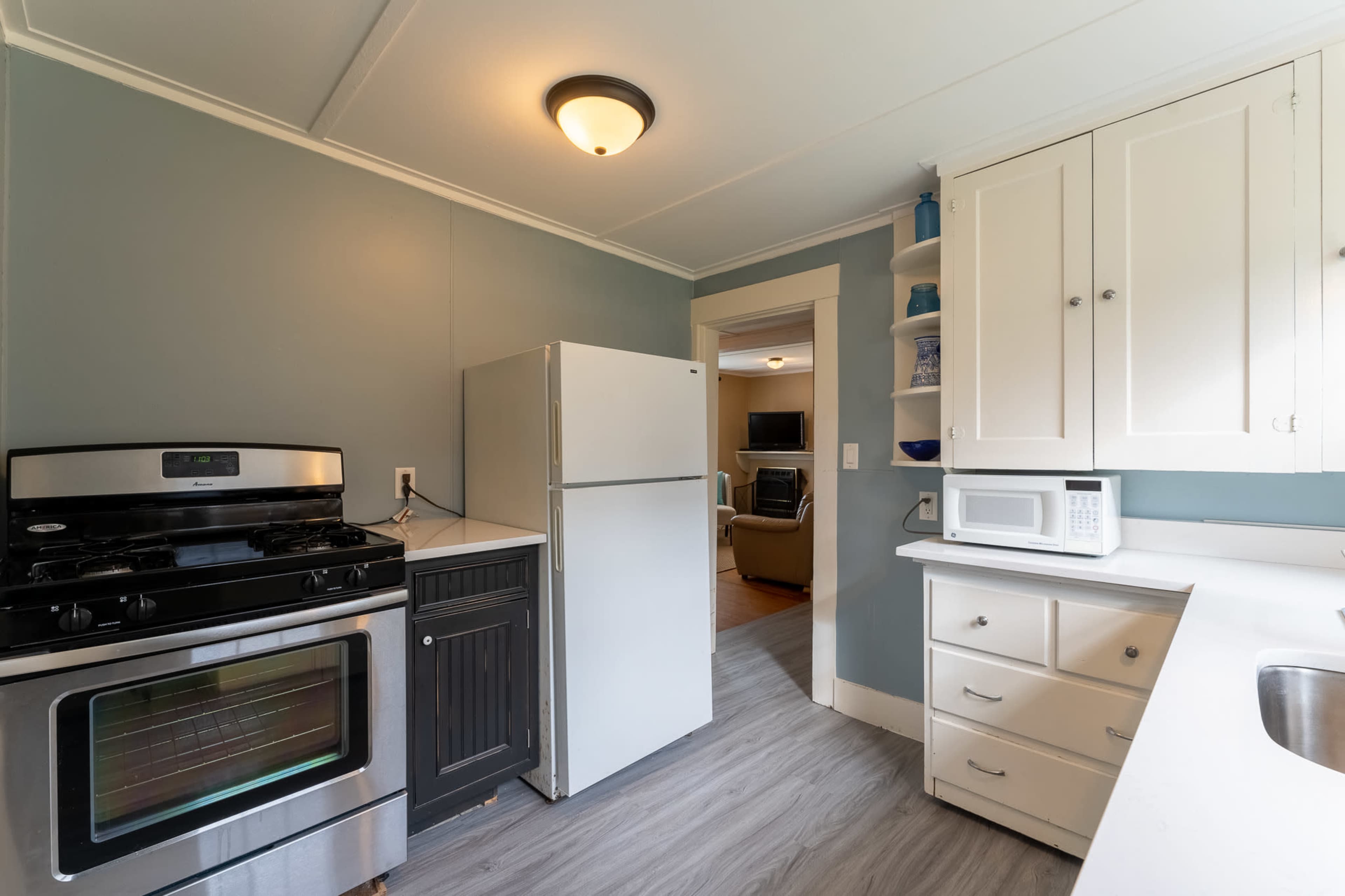 A compact kitchen featuring a stainless steel stove, a white refrigerator, and white cabinetry against a light blue wall.